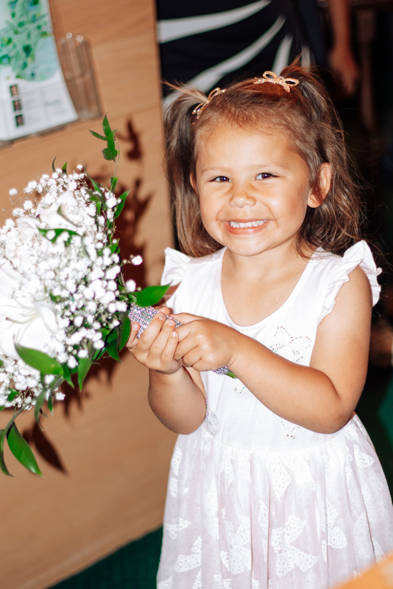 Smiling young flower girl in white dress holding wedding bouquet with baby's breath flowers.
