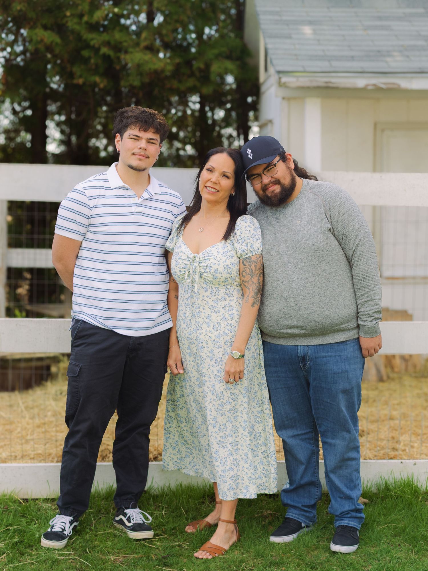 Family of three smiling together outdoors near a white fence on a green lawn.