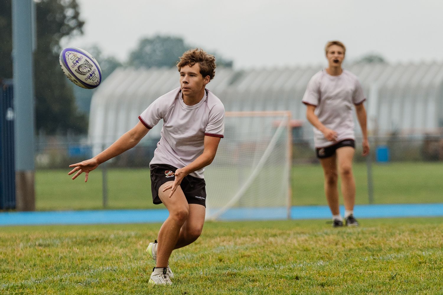Young male rugby player passes ball during outdoor practice on green field on cloudy day.
