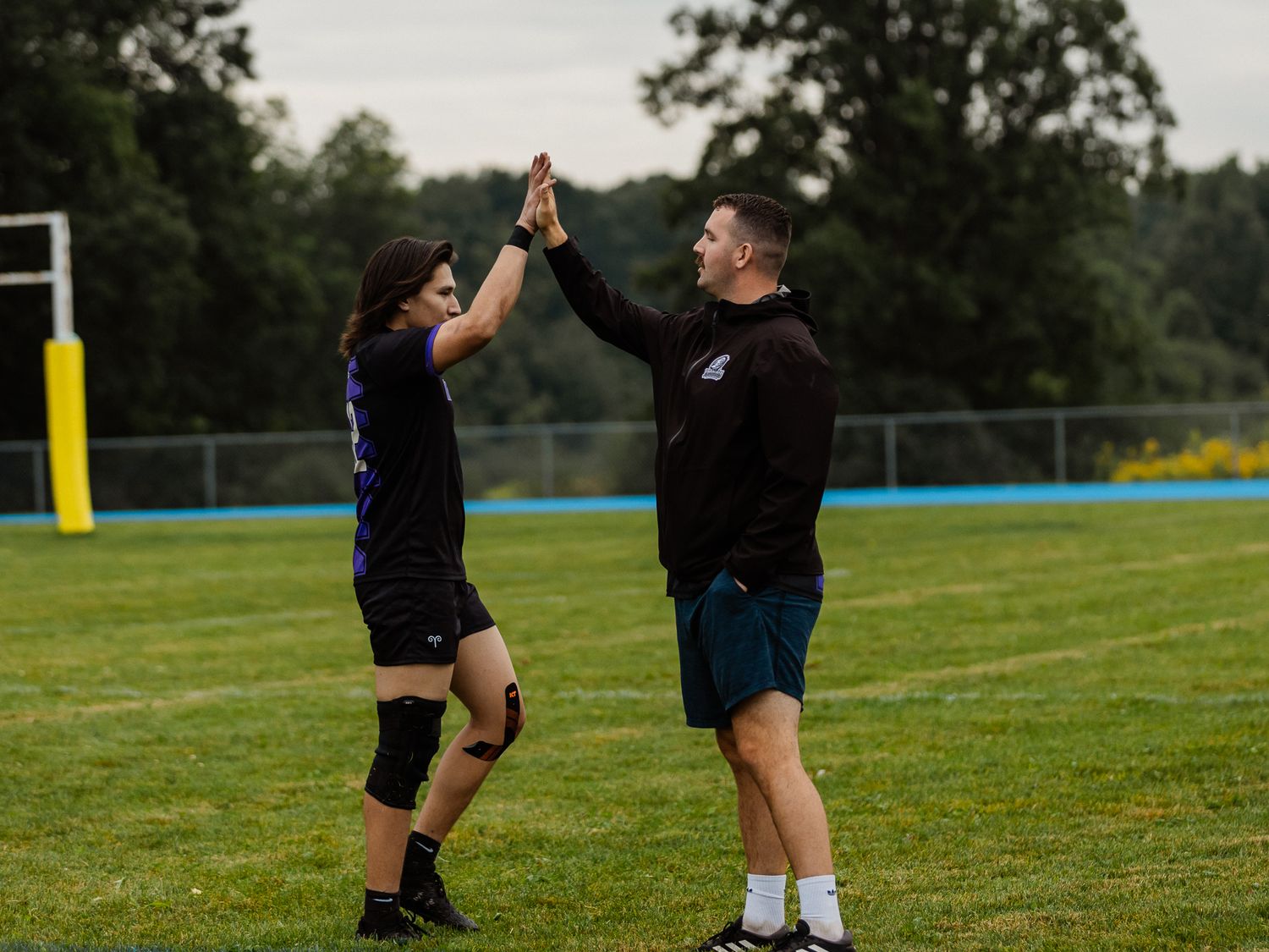 Two rugby players celebrate with a high five on a green sports field after a successful game.