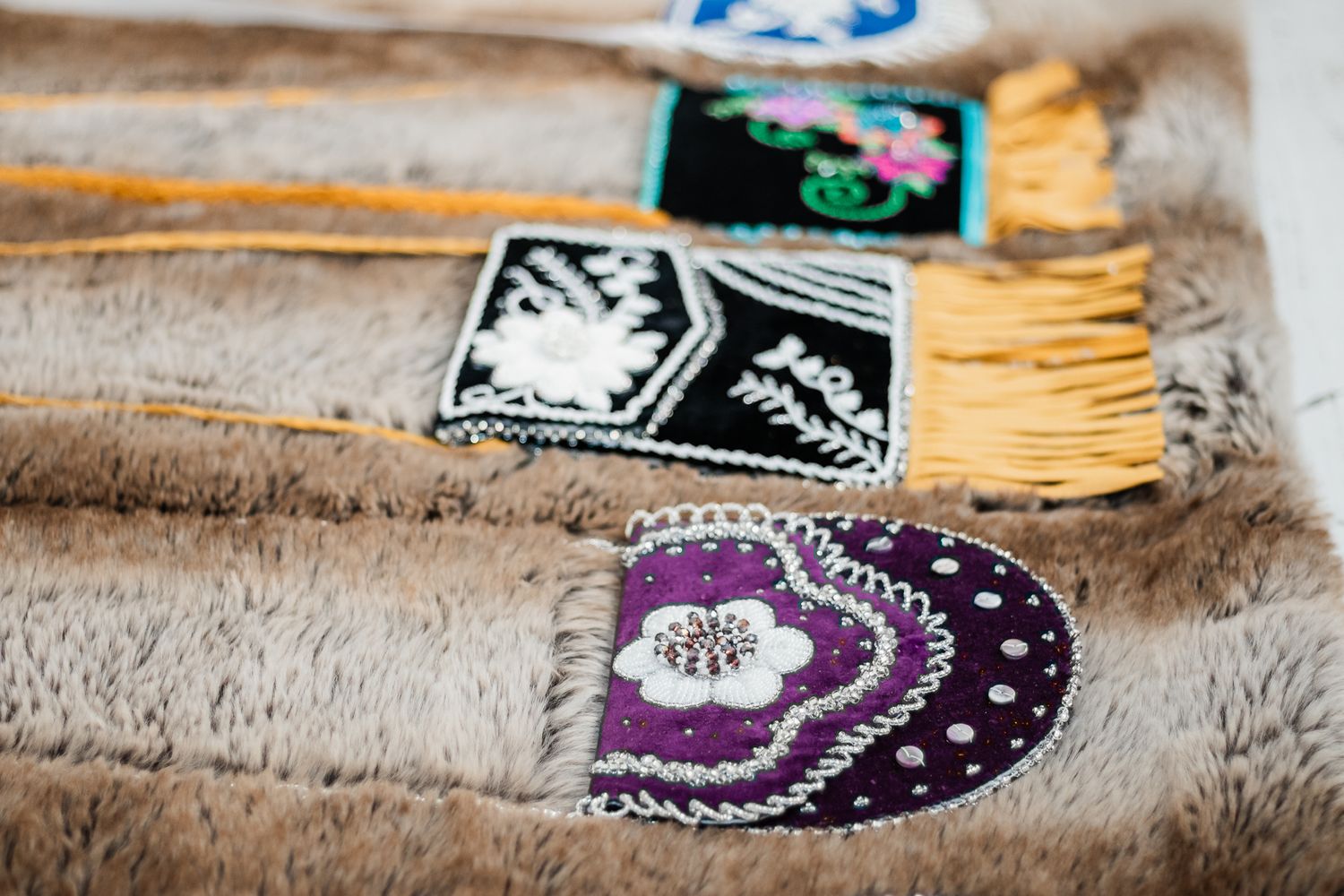 Handcrafted Indigenous beaded mittens and embroidered pouches with fringe displayed on fur textile.