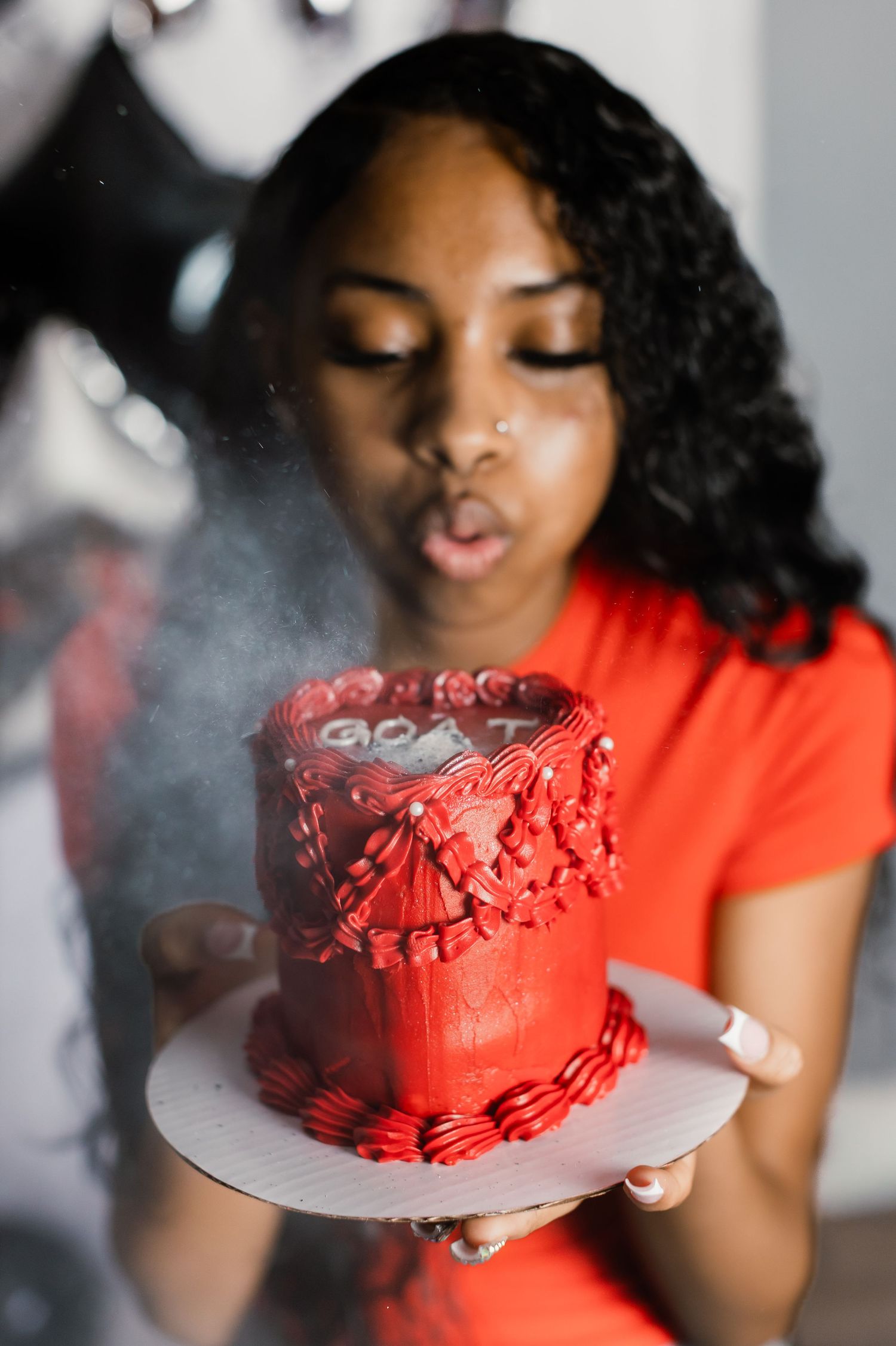 Red birthday cake being presented with smoke effects in a stylized photo shoot.