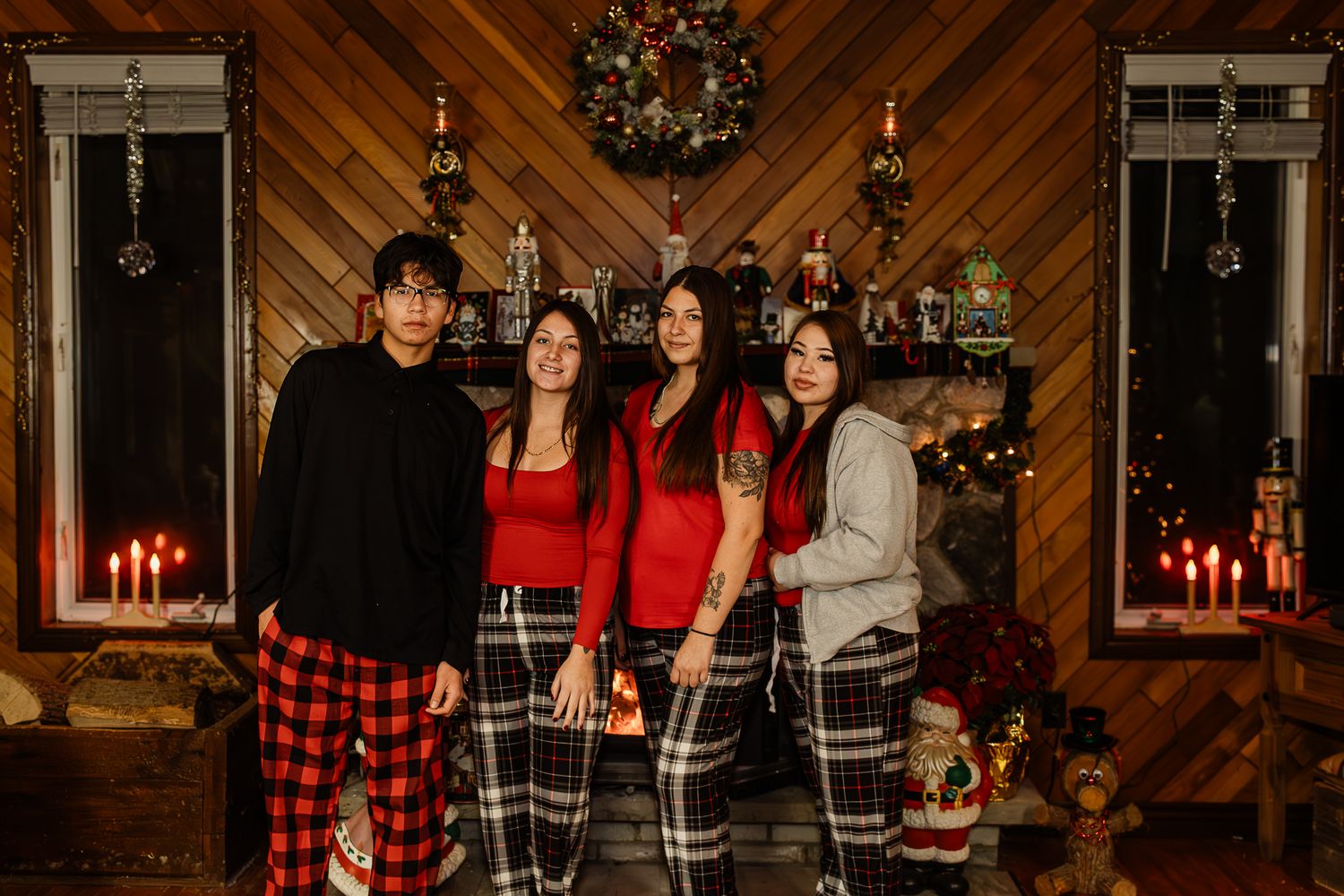 Family wearing matching buffalo plaid pajamas pose in front of decorated Christmas tree and fireplace.