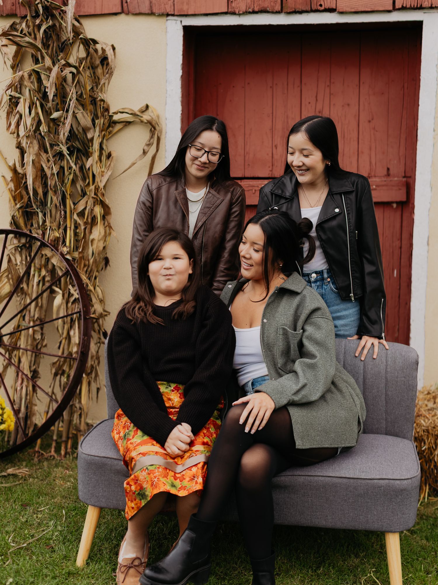 Friends sharing joyful moments while sitting on a bench against a rustic red barn backdrop.