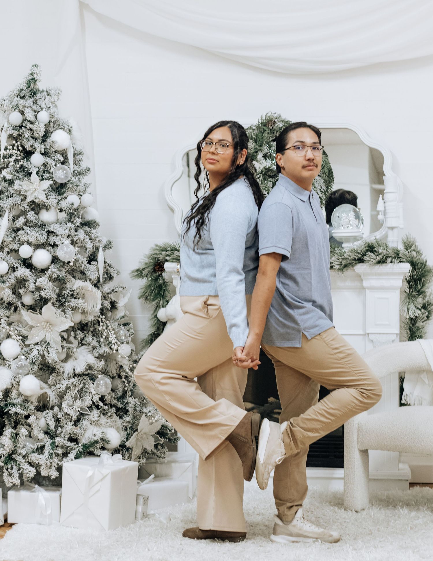 Two people strike dynamic poses in coordinated casual outfits against a white Christmas backdrop.