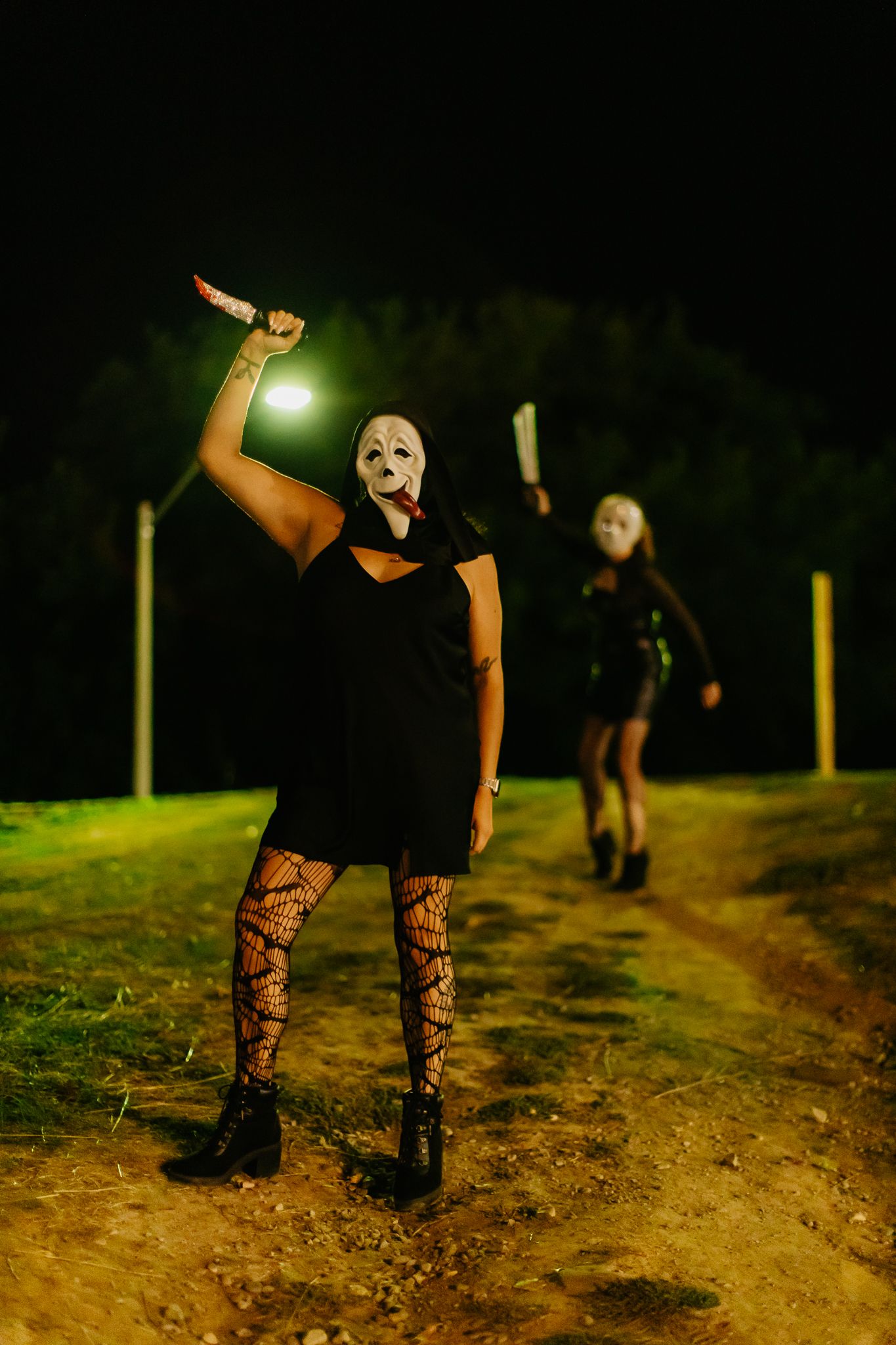 Masked figures in gothic attire posing on dirt path under night sky.