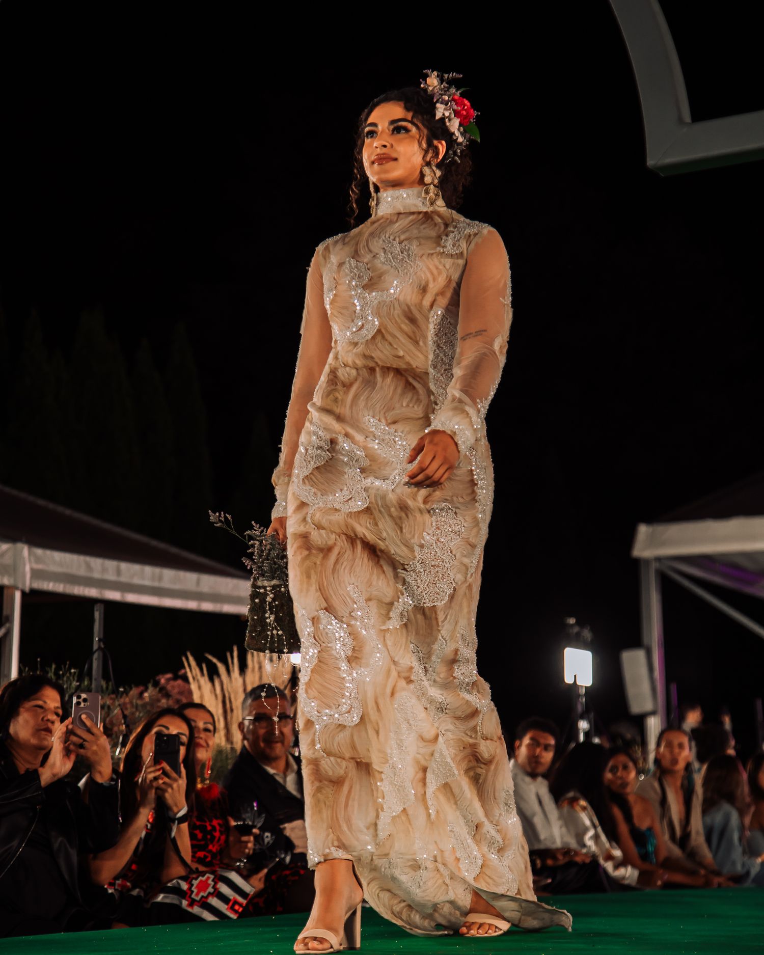 Models showcase delicate lace dresses on an illuminated runway during a nighttime fashion show.