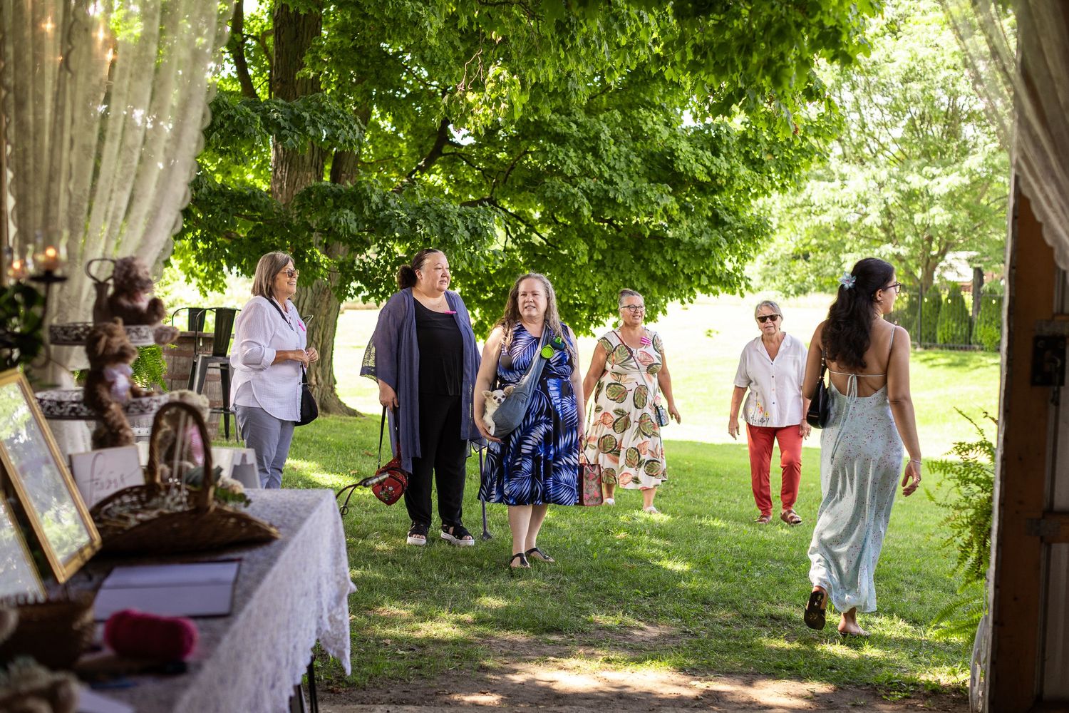 Guests walking through an outdoor garden path at an event with white decor and green trees.