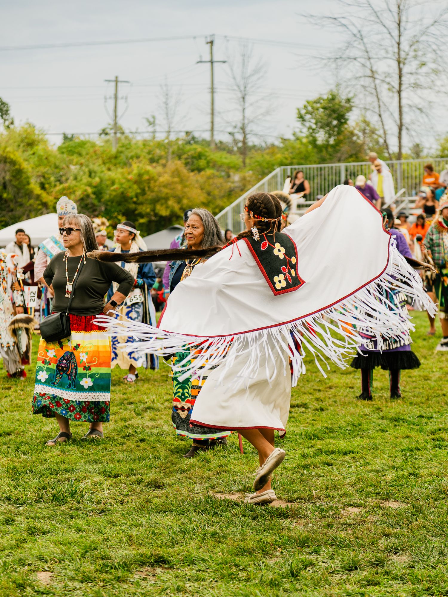 Traditional dancers spinning and displaying white fringed shawls during a powwow performance.