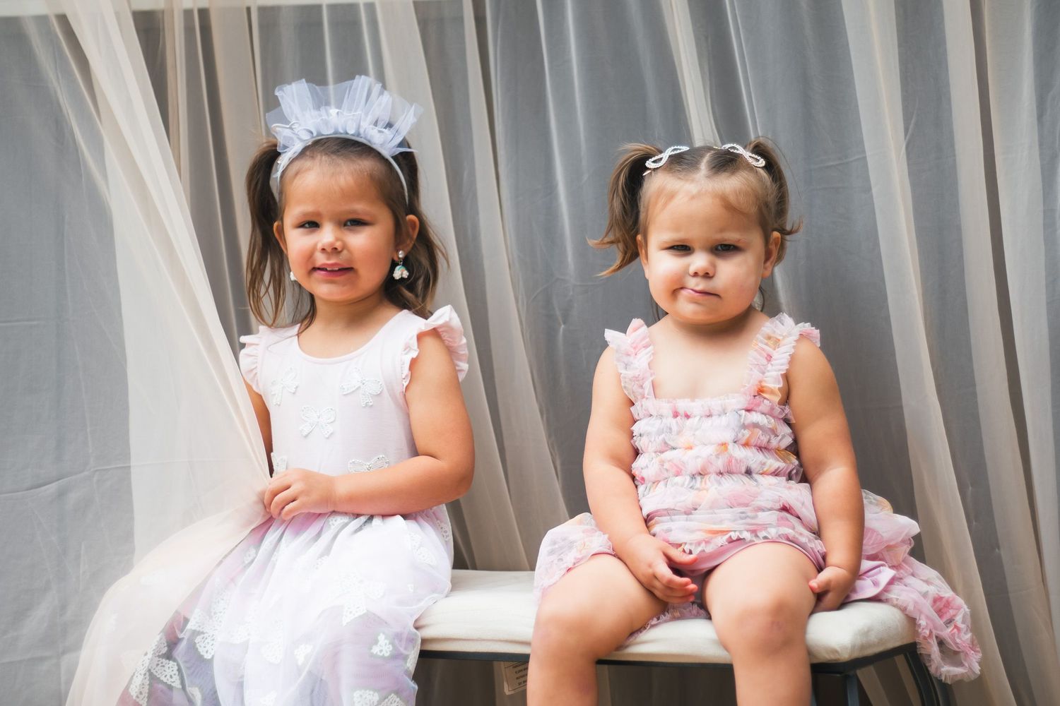 Young flower girls in white and pink dresses sit together at a wedding event.