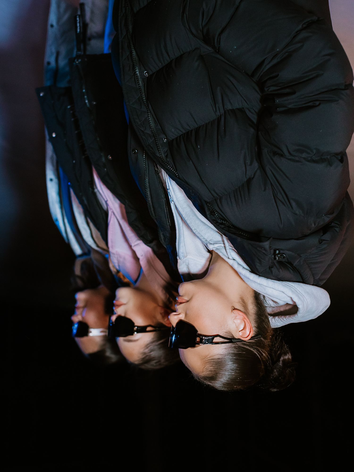 Close-up of three models in puffer jackets and shield sunglasses photographed from below at night.