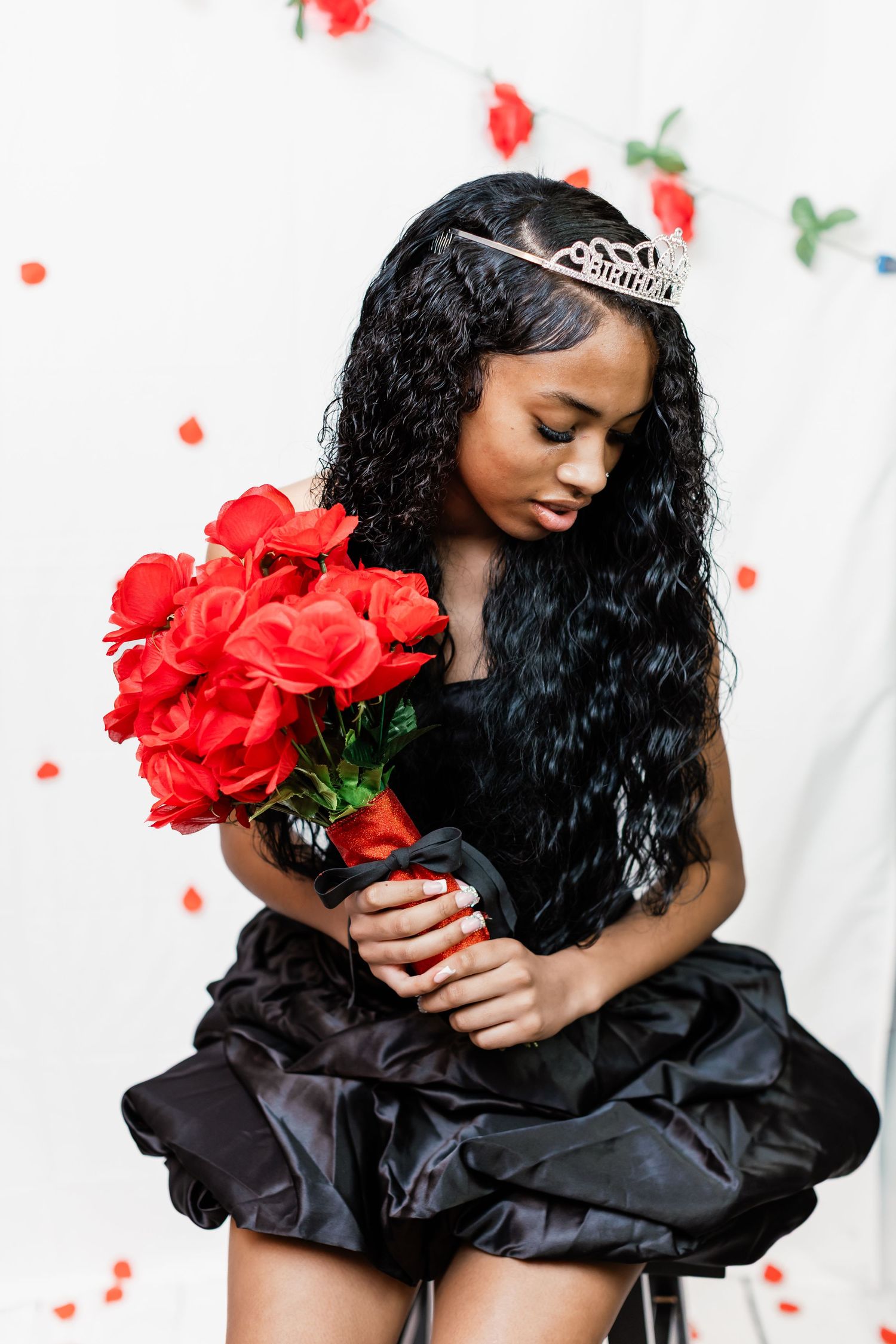 Elegant portrait session with red roses and black formal dress against white background.