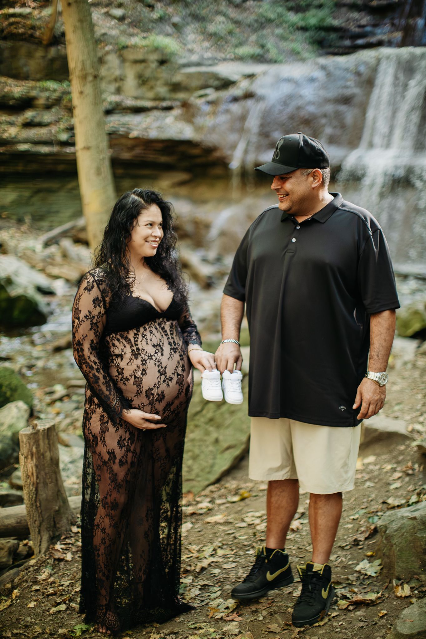 A couple shares joyful moments during their maternity photoshoot by a cascading waterfall.