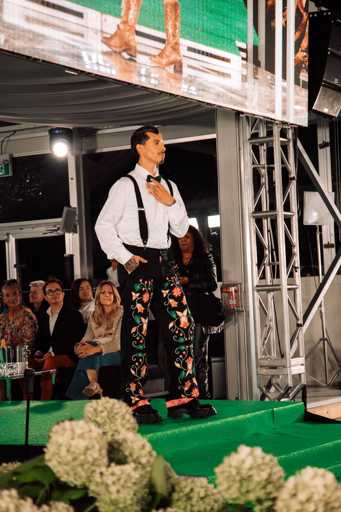 Performers in formal black and white attire dance on a green-lit stage with hydrangea decorations.