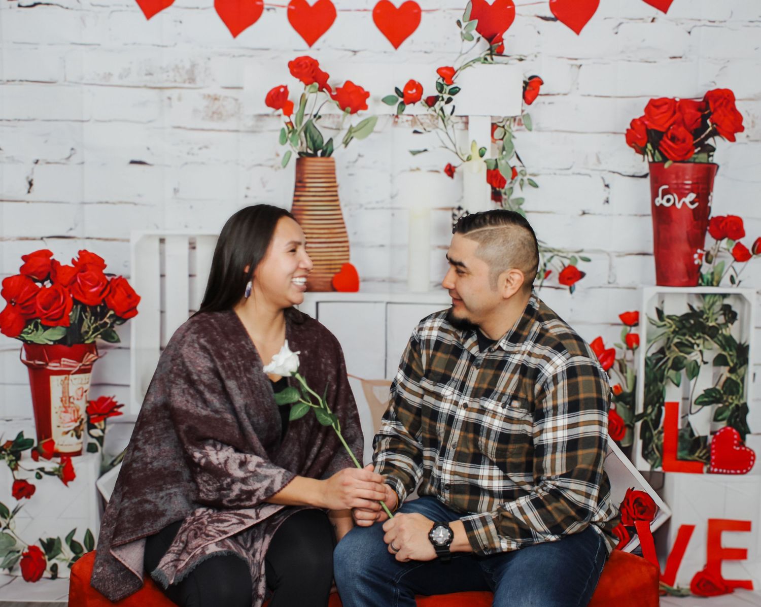 Valentine's day photo session with red hearts and roses against white brick wall backdrop.