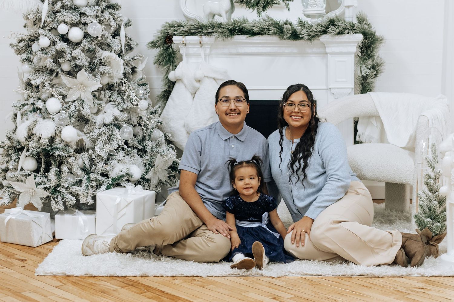 Family photo session with festive white Christmas trees and fireplace decorations in the background.