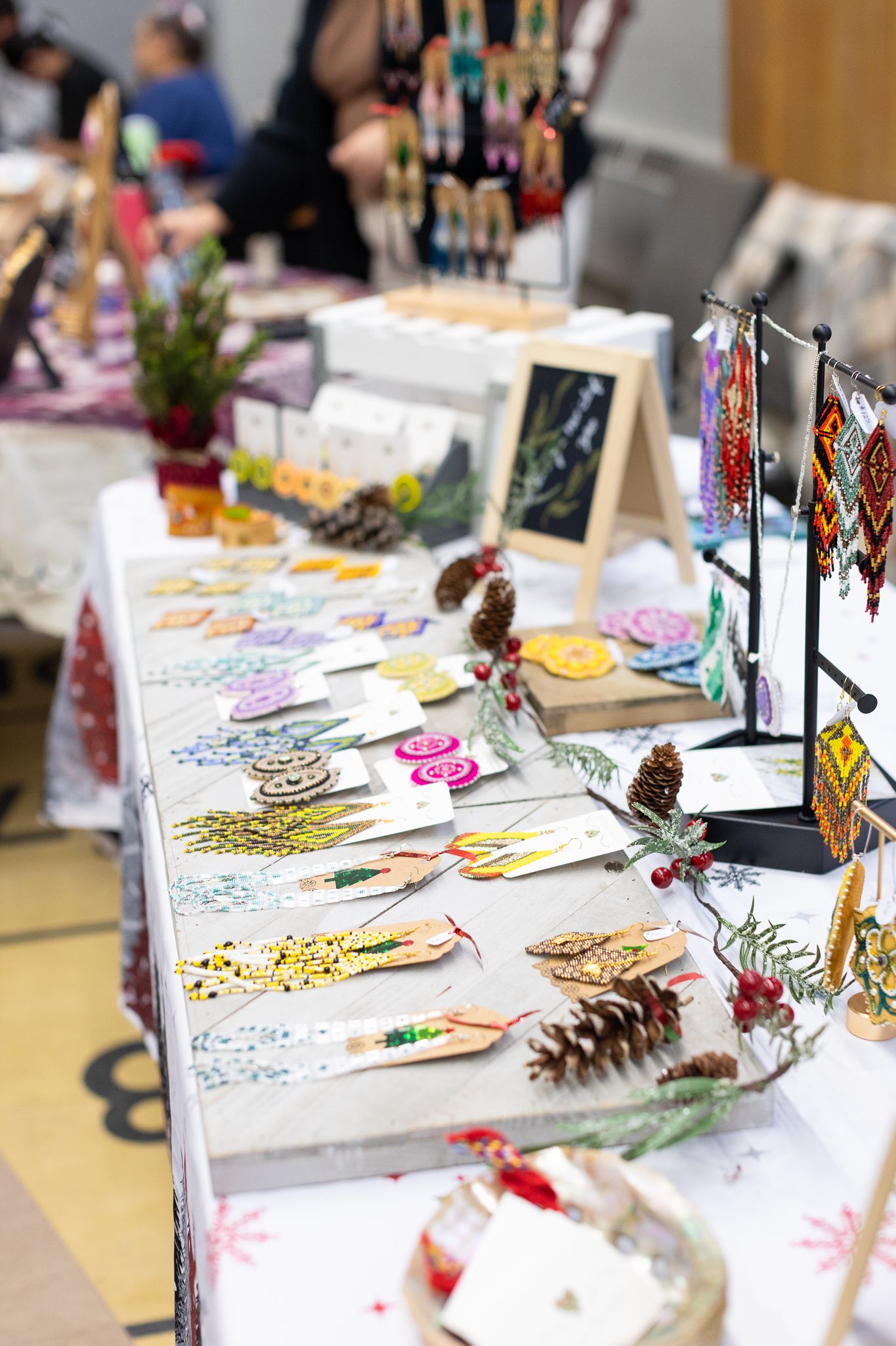 Handmade craft items and artwork displayed on white tables at a holiday market or craft fair.