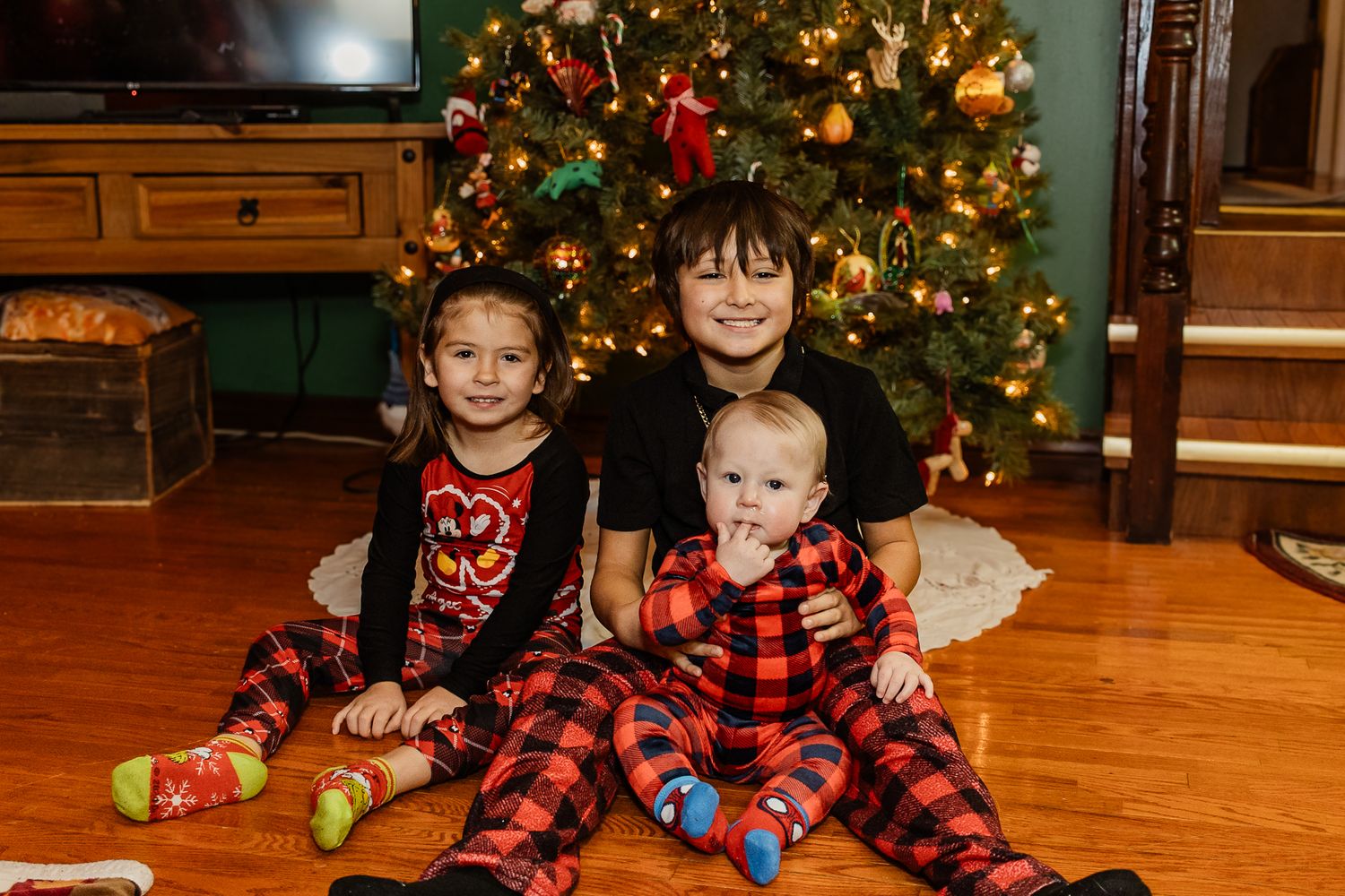 Group photo in front of illuminated Christmas tree with wood paneled walls and holiday decorations.