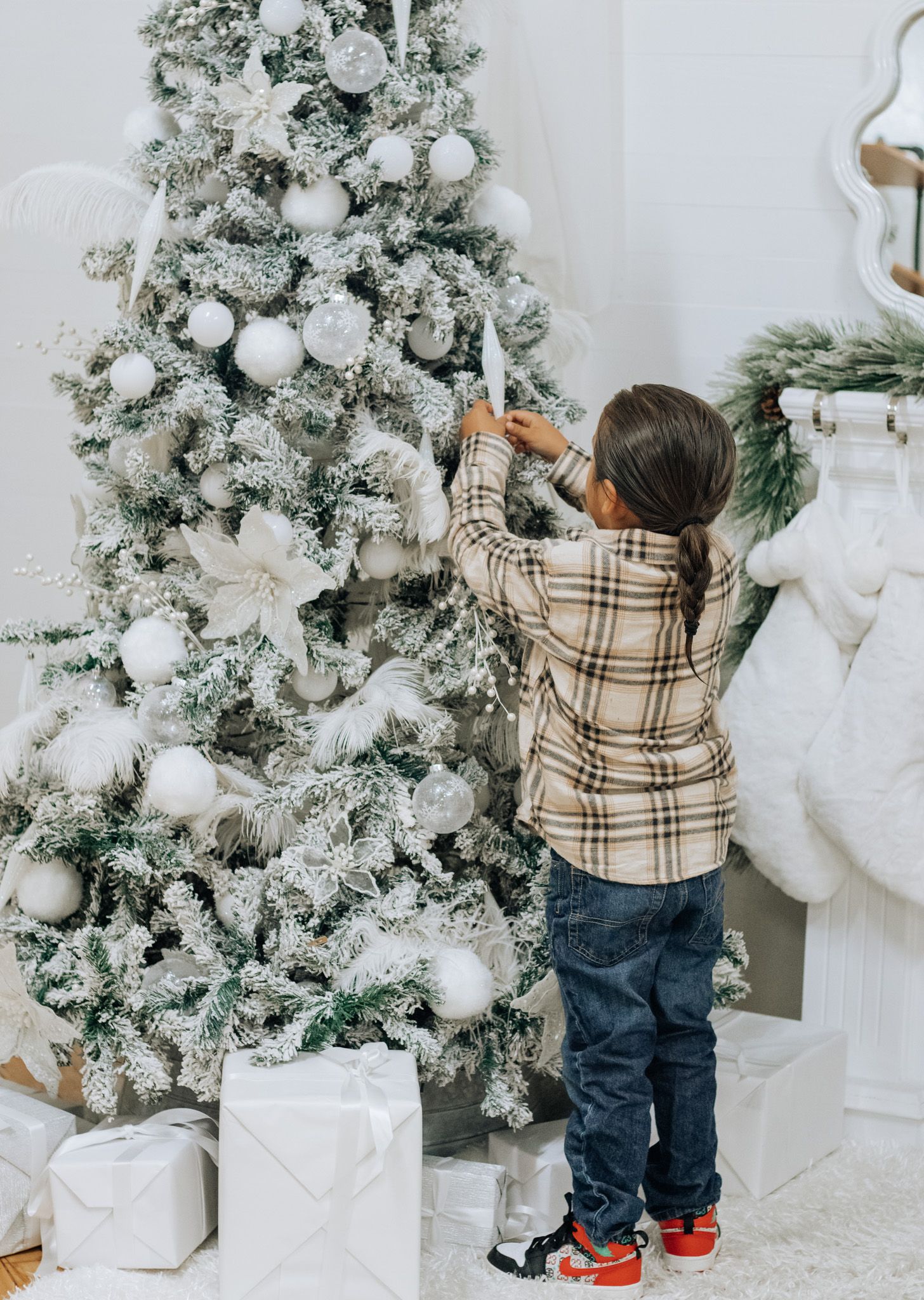 Small child reaching for ornaments on elegant white Christmas tree during holiday photo shoot.