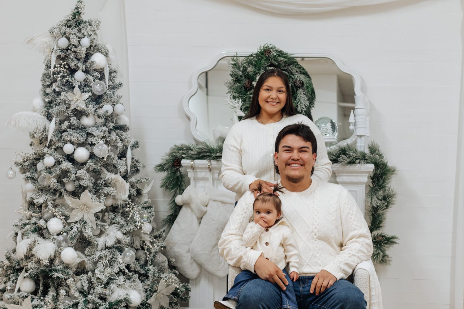 Family gathered for holiday portraits with white Christmas trees and decorative fireplace setting.