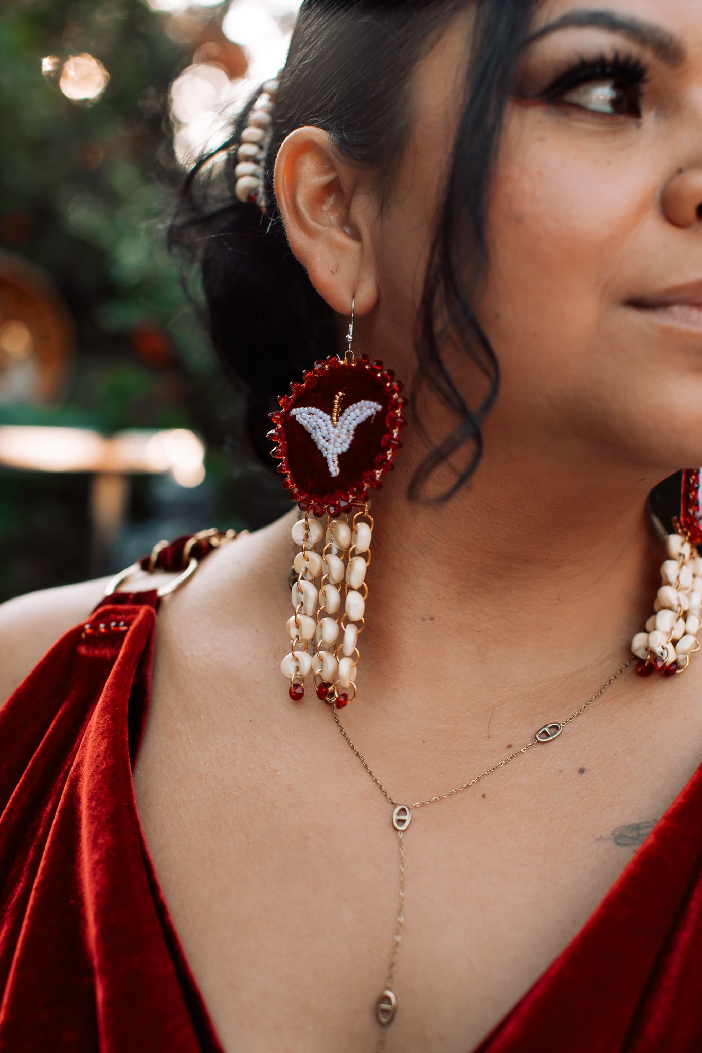 Woman wearing ornate red velvet earrings with pearl tassels and a delicate gold necklace.