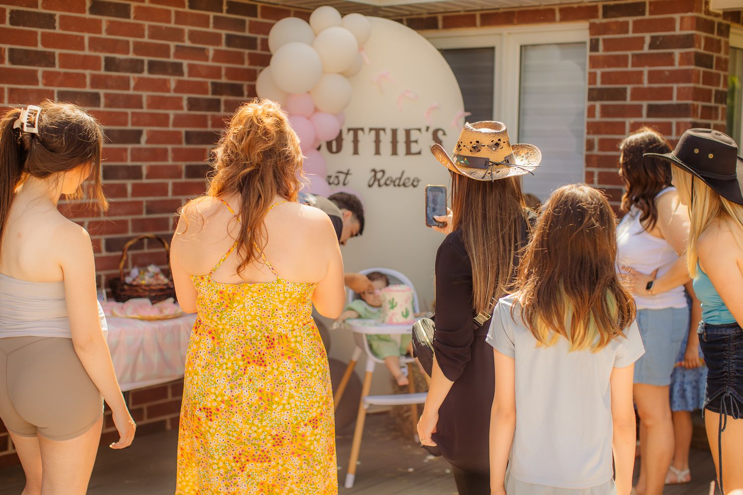 Group of women gathered outdoors at a bachelorette party with balloon arch and rustic western theme decor.
