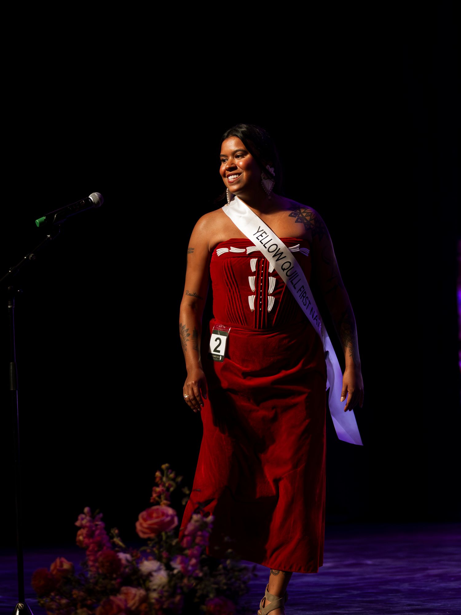 A contestant in a red strapless jumpsuit wearing a Yellow County sash performs on a pageant stage.