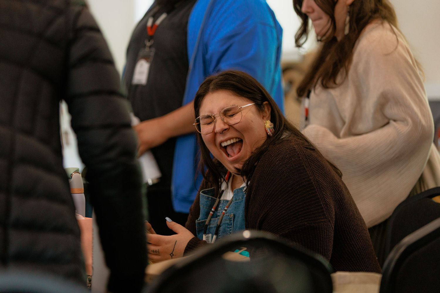 A woman laughs joyfully during a group gathering or conference event indoors.