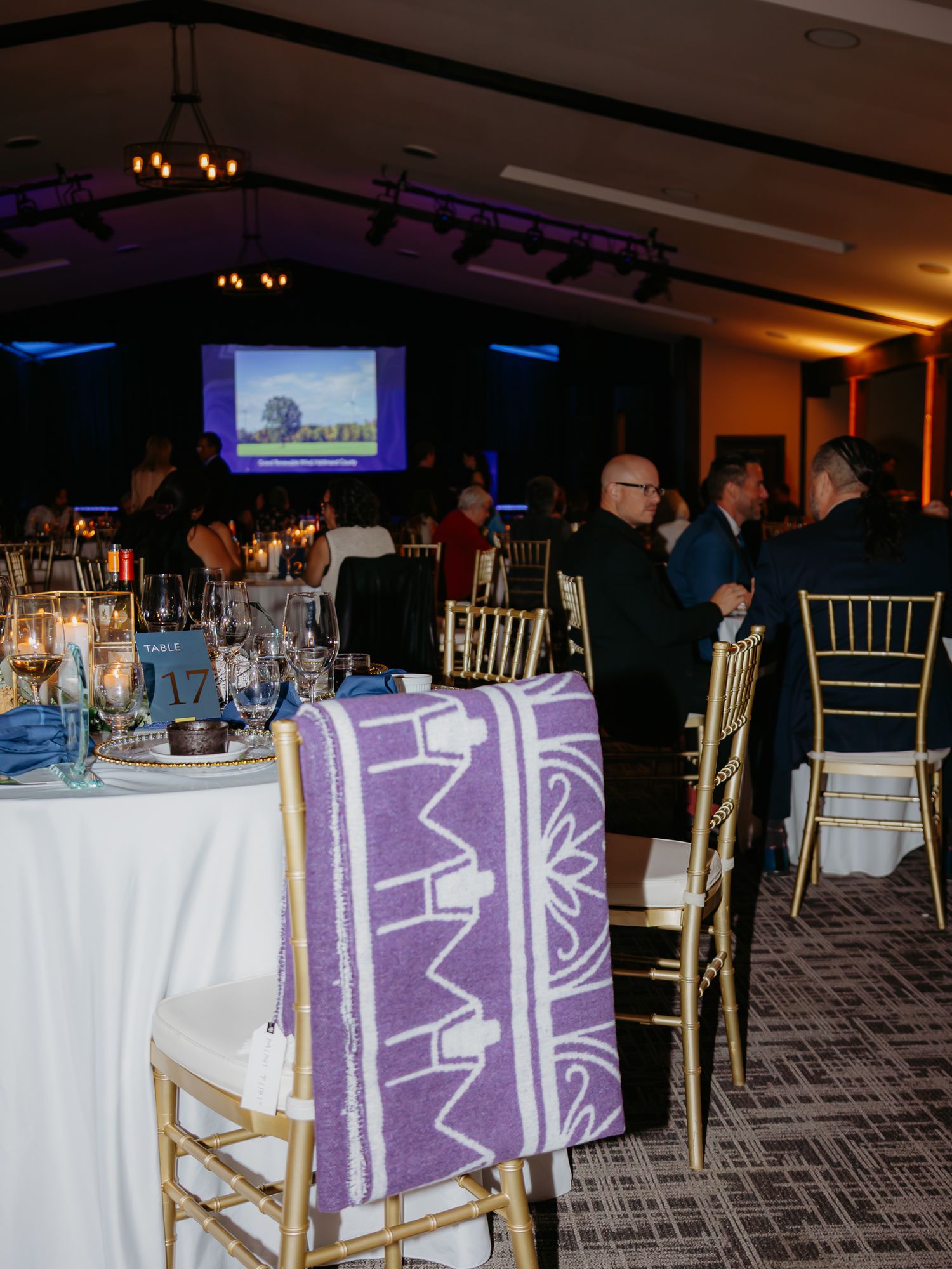 Elegant banquet hall with gold chiavari chairs, blue table settings, and a purple patterned blanket draped over a chair during a gala event.