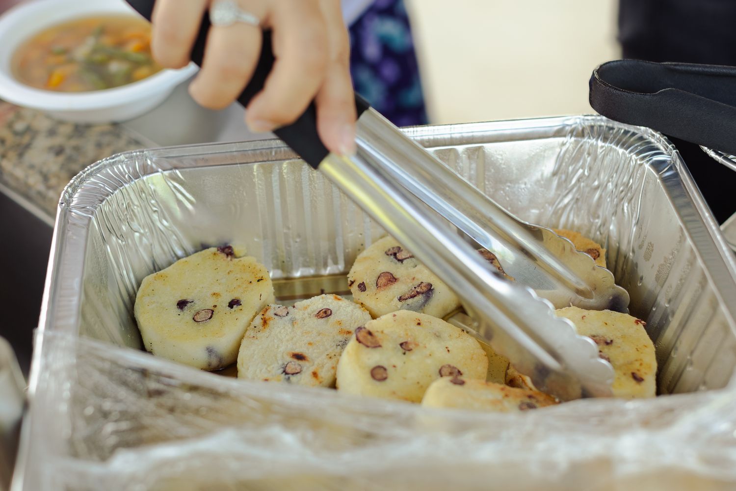 Tongs serving round cranberry scones in a foil tray at a buffet event.