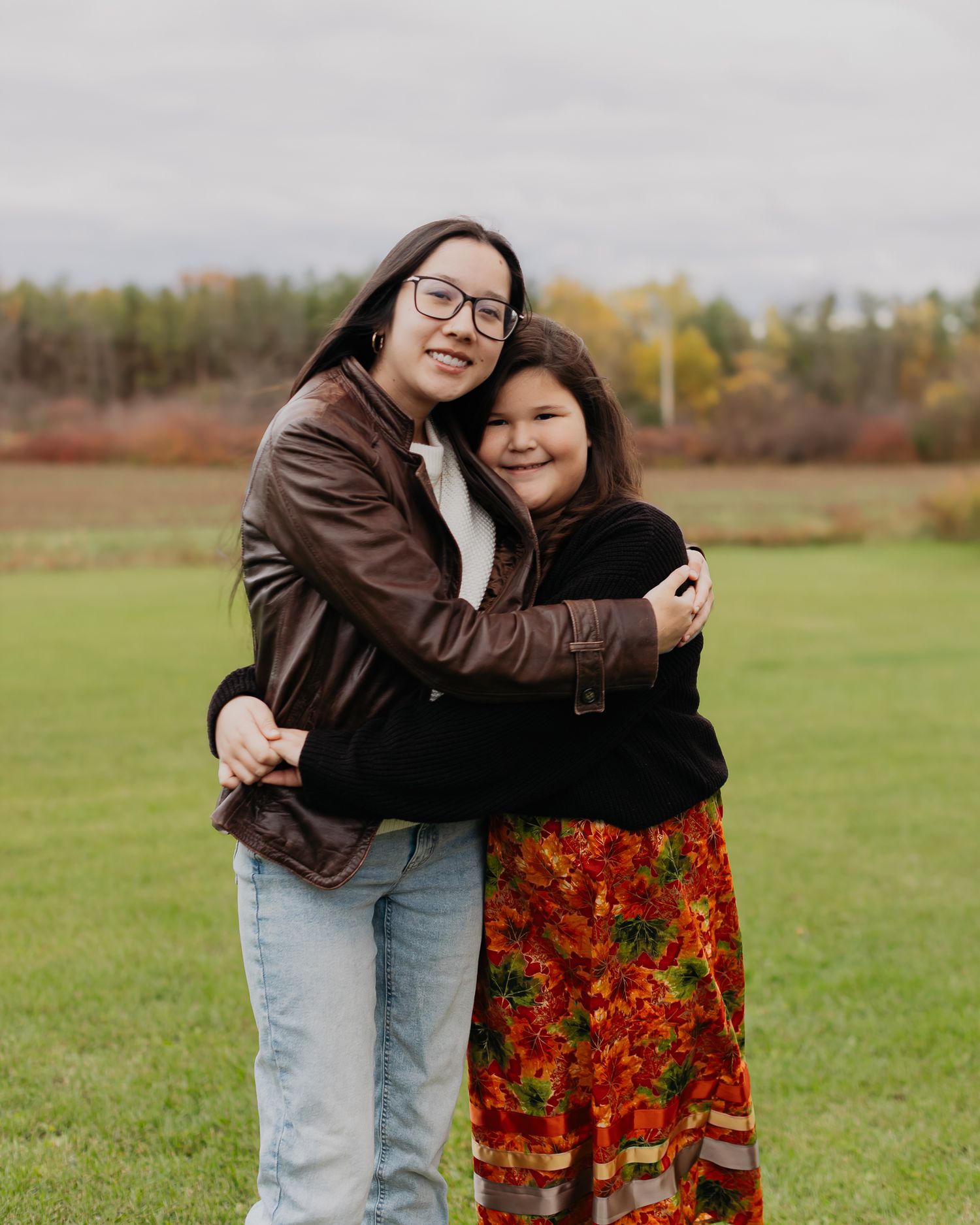 A candid outdoor photoshoot showing warm embraces and laughter in a grassy field during autumn.
