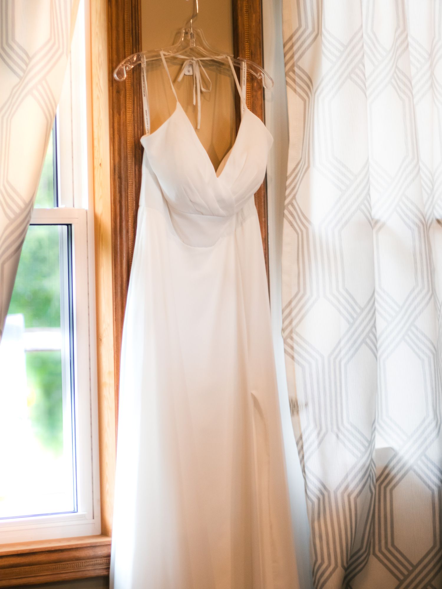 White wedding dresses hanging on display against a patterned wallpaper background.