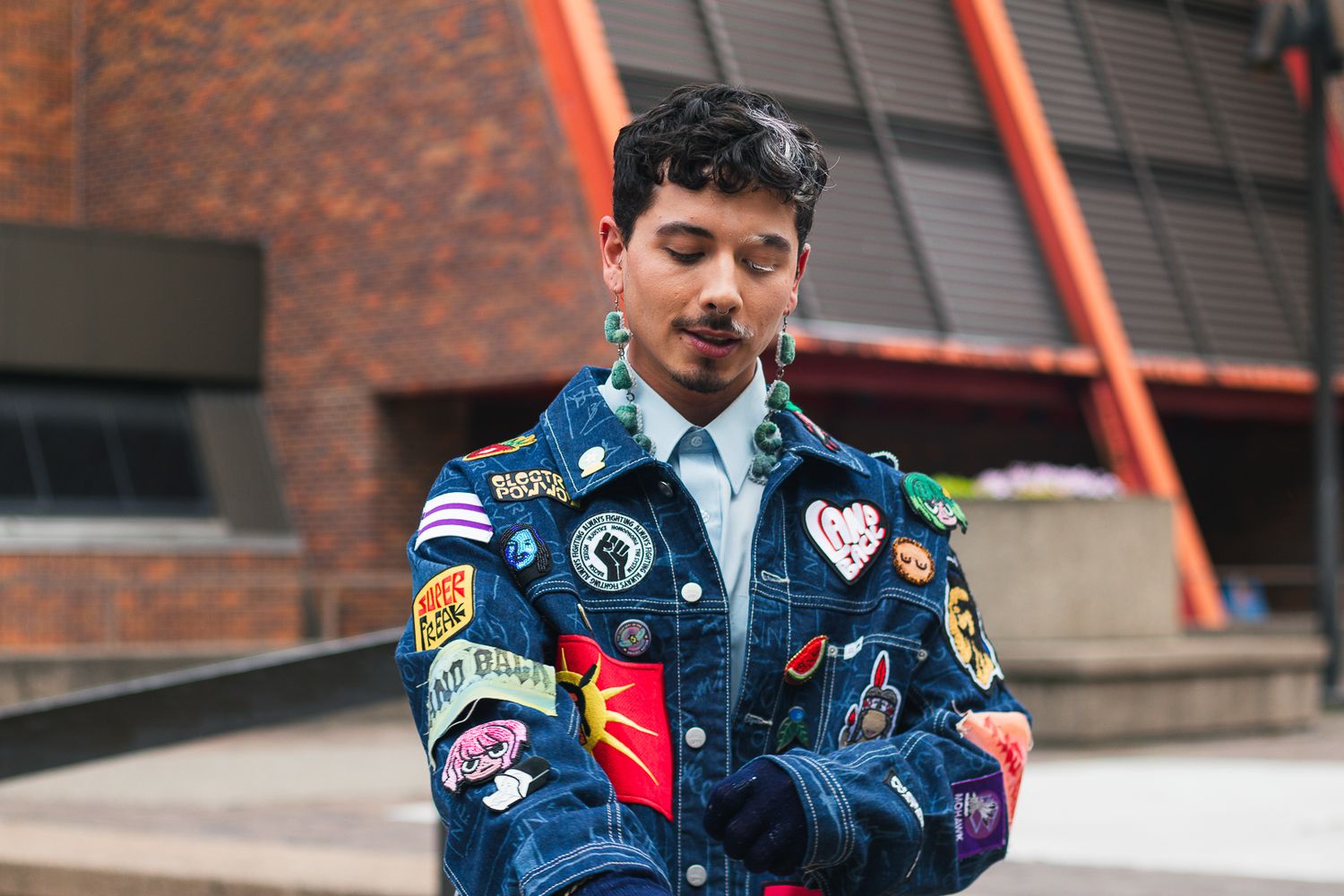 Person wearing a denim jacket decorated with various patches and pins.