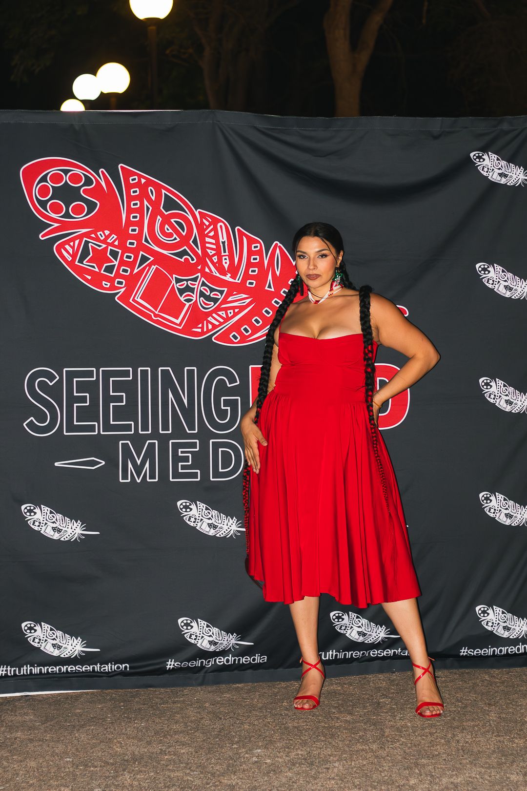 Red dress against backdrop with white feather designs and red logo.