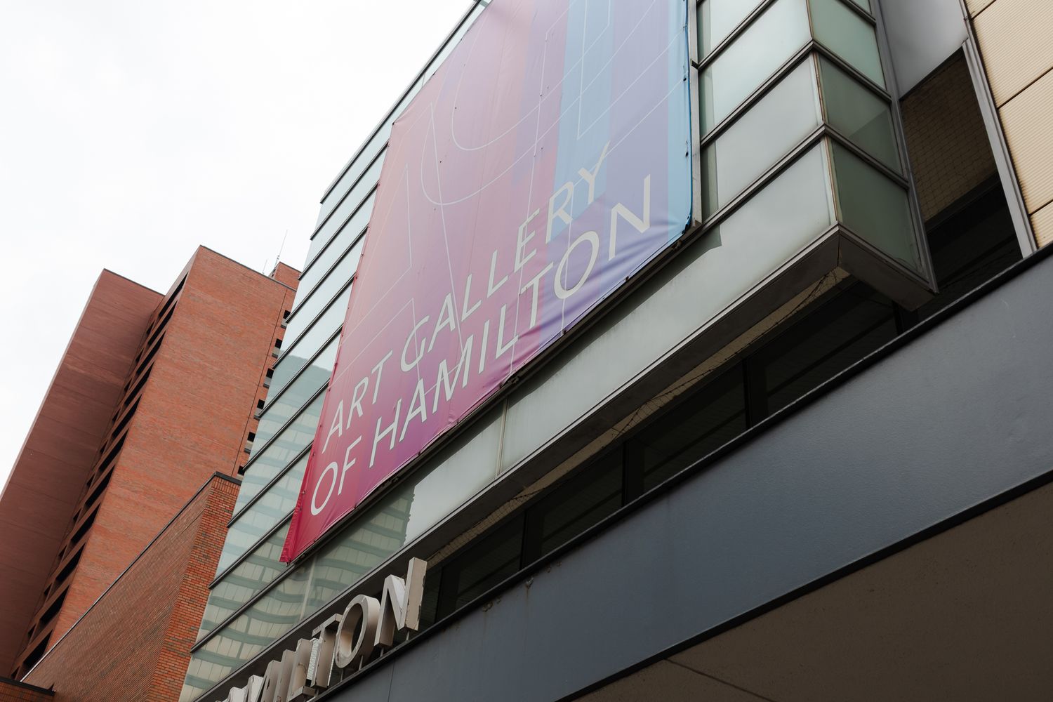 Exterior view of the Art Gallery of Hamilton building with large pink and red signage on the facade.