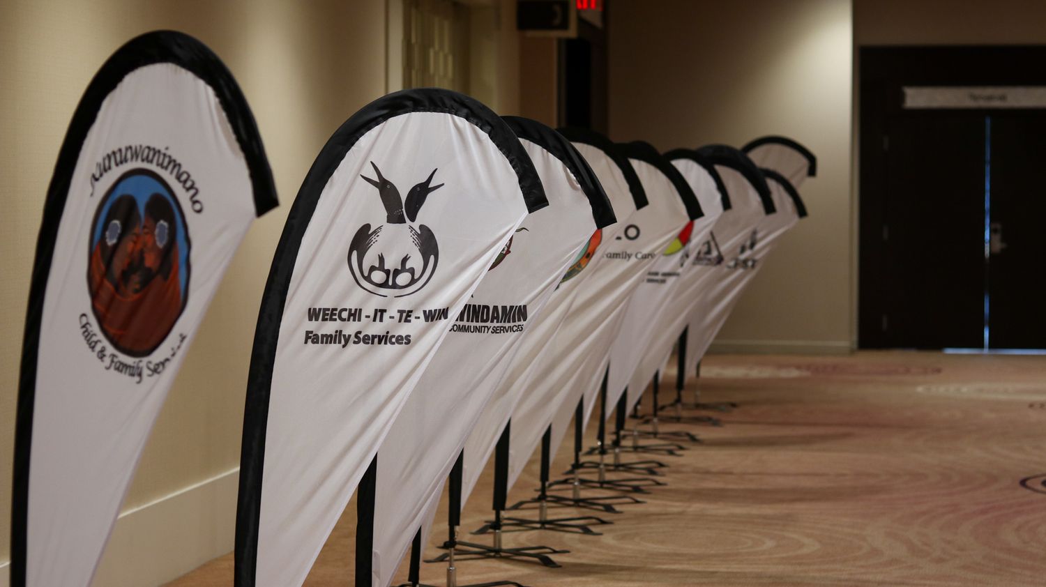 Row of standing banners with indigenous artwork and organizational branding in a conference space.