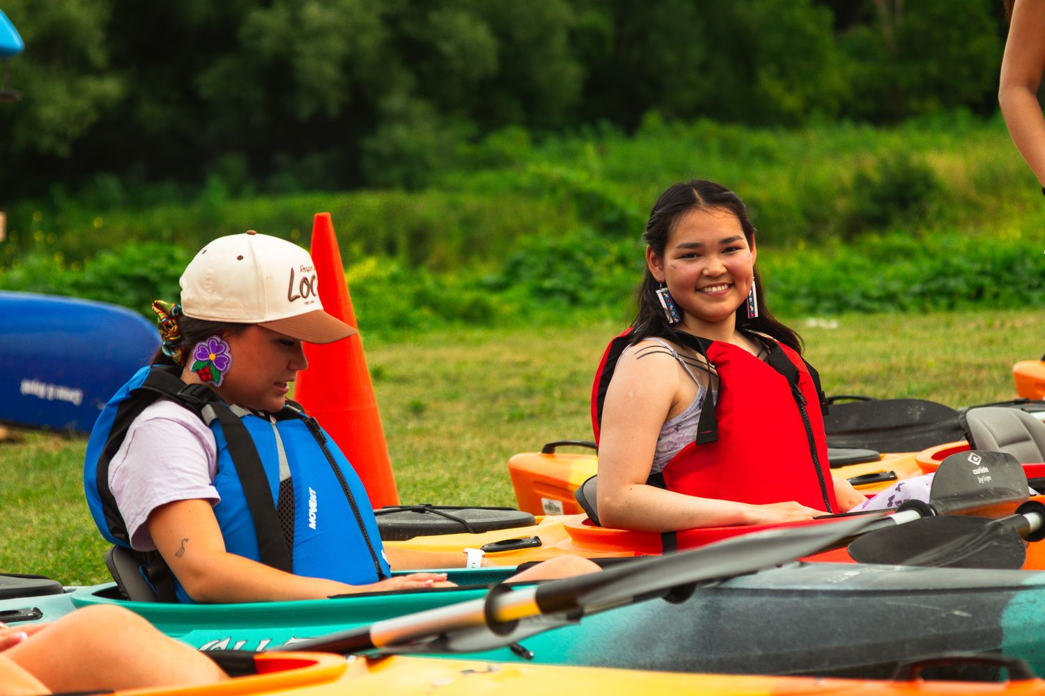 Two kayakers smile while paddling on calm waters surrounded by greenery.