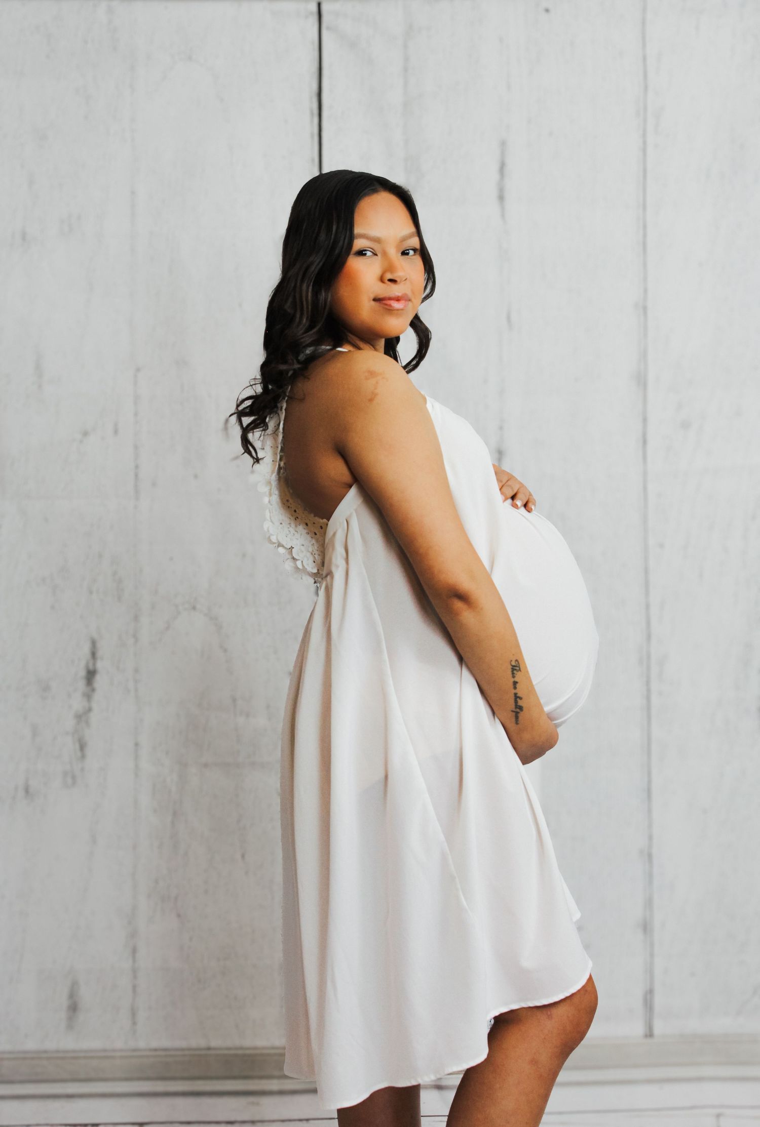Elegant maternity photoshoot featuring flowing white fabric against minimalist background.