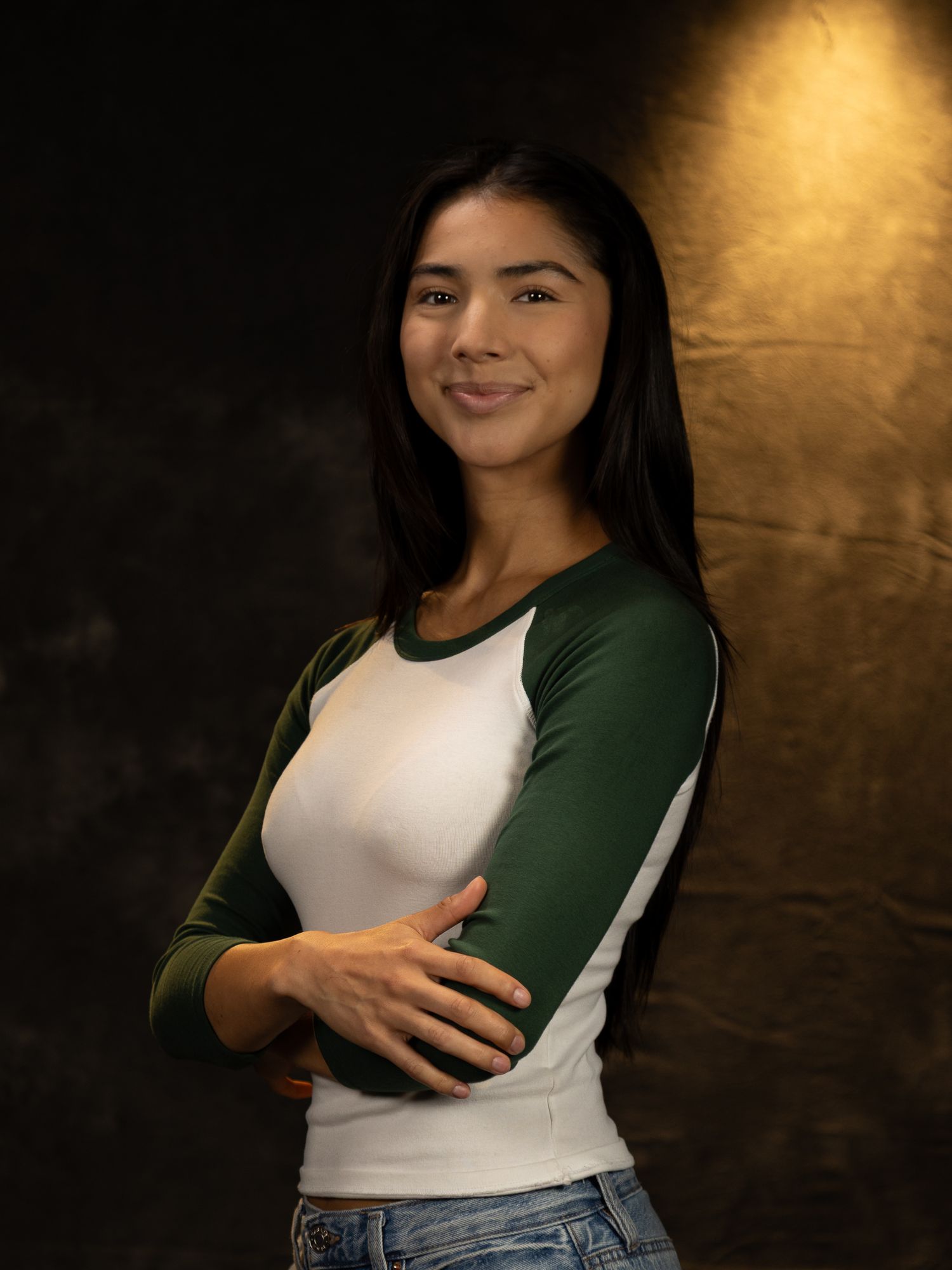 Portrait of person wearing green and white raglan shirt against dramatic dark background.