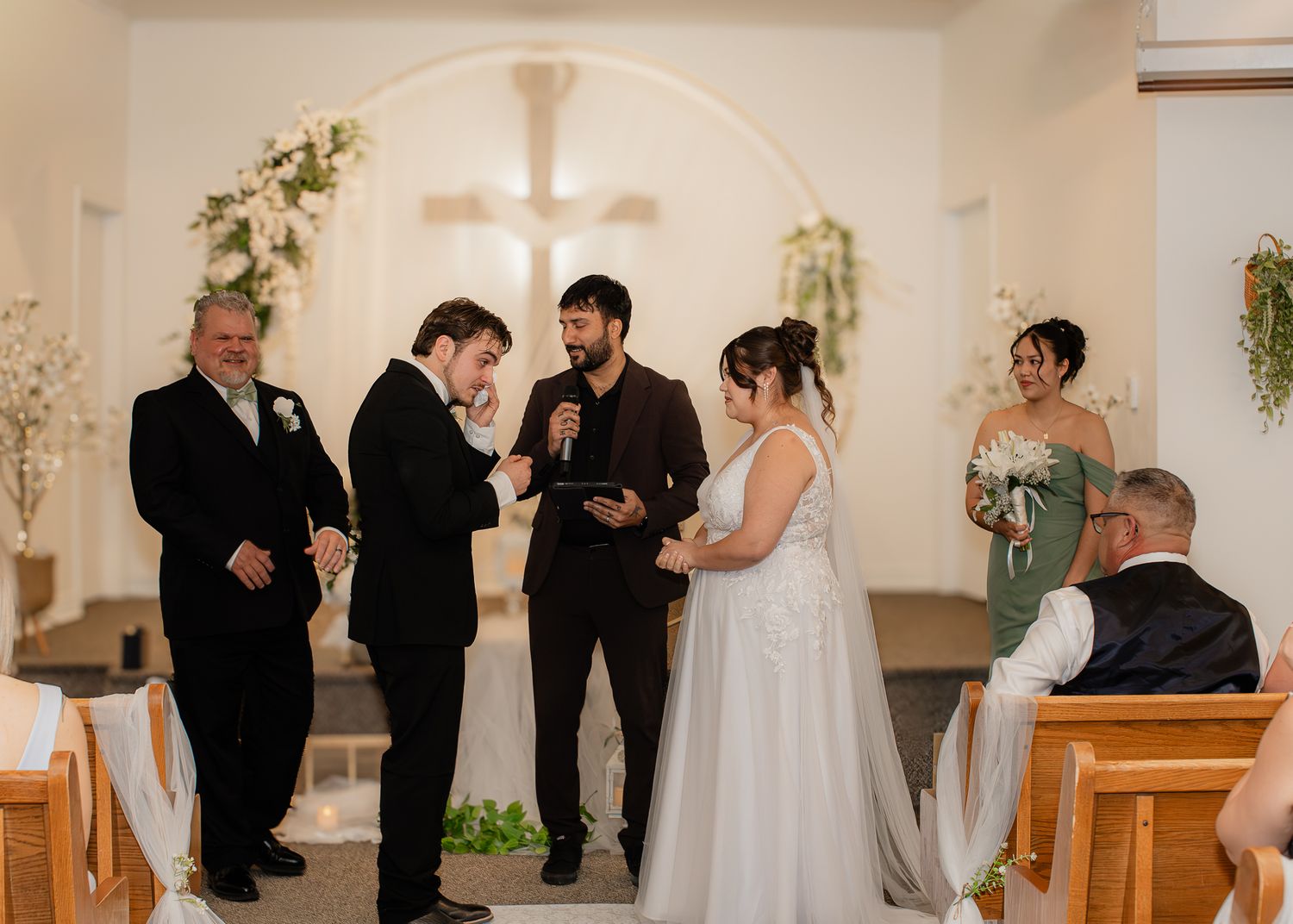 Bride and groom exchange vows at a church wedding ceremony with officiant and wedding party.