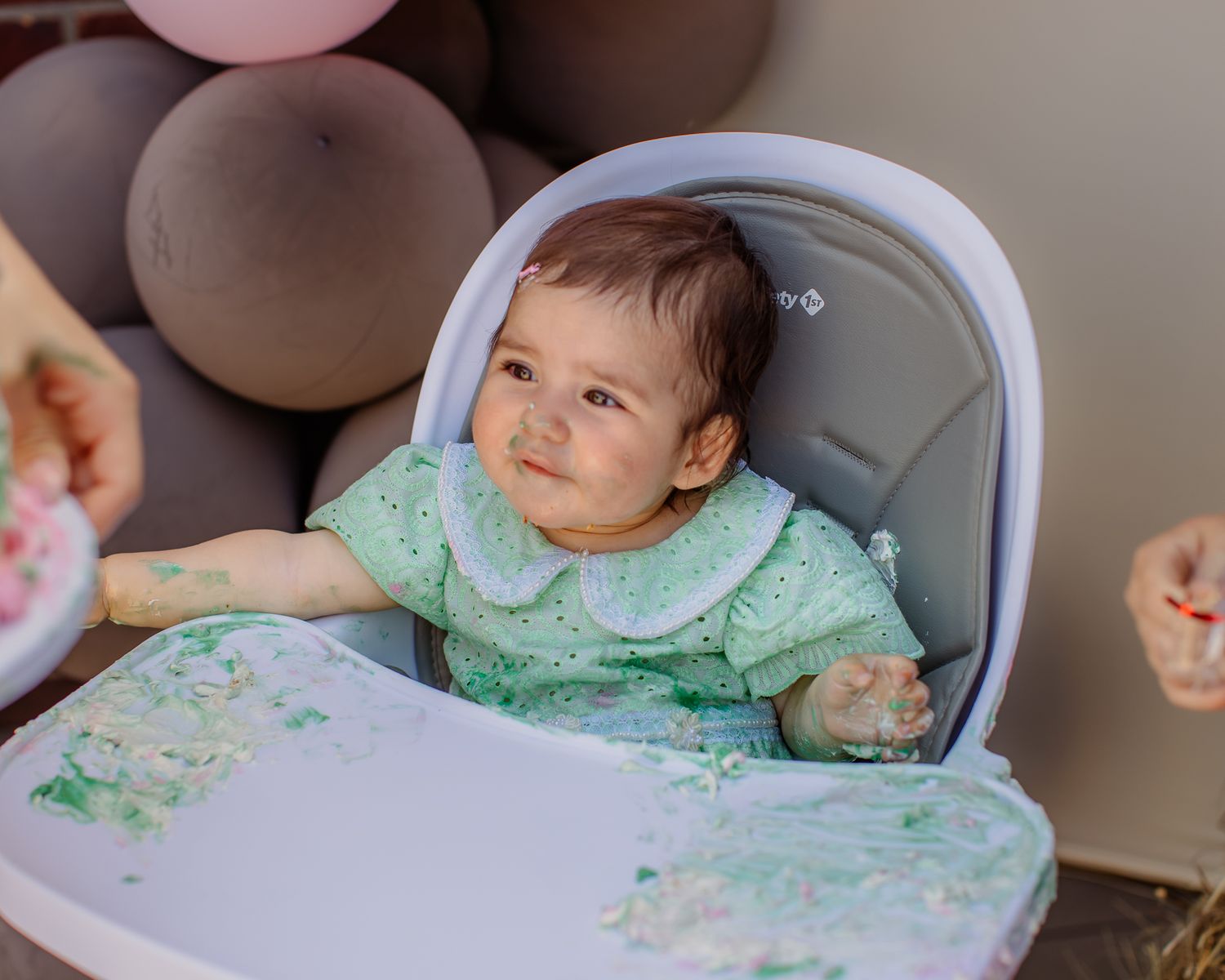 Baby girl in high chair with cake smash mess at first birthday party celebration.