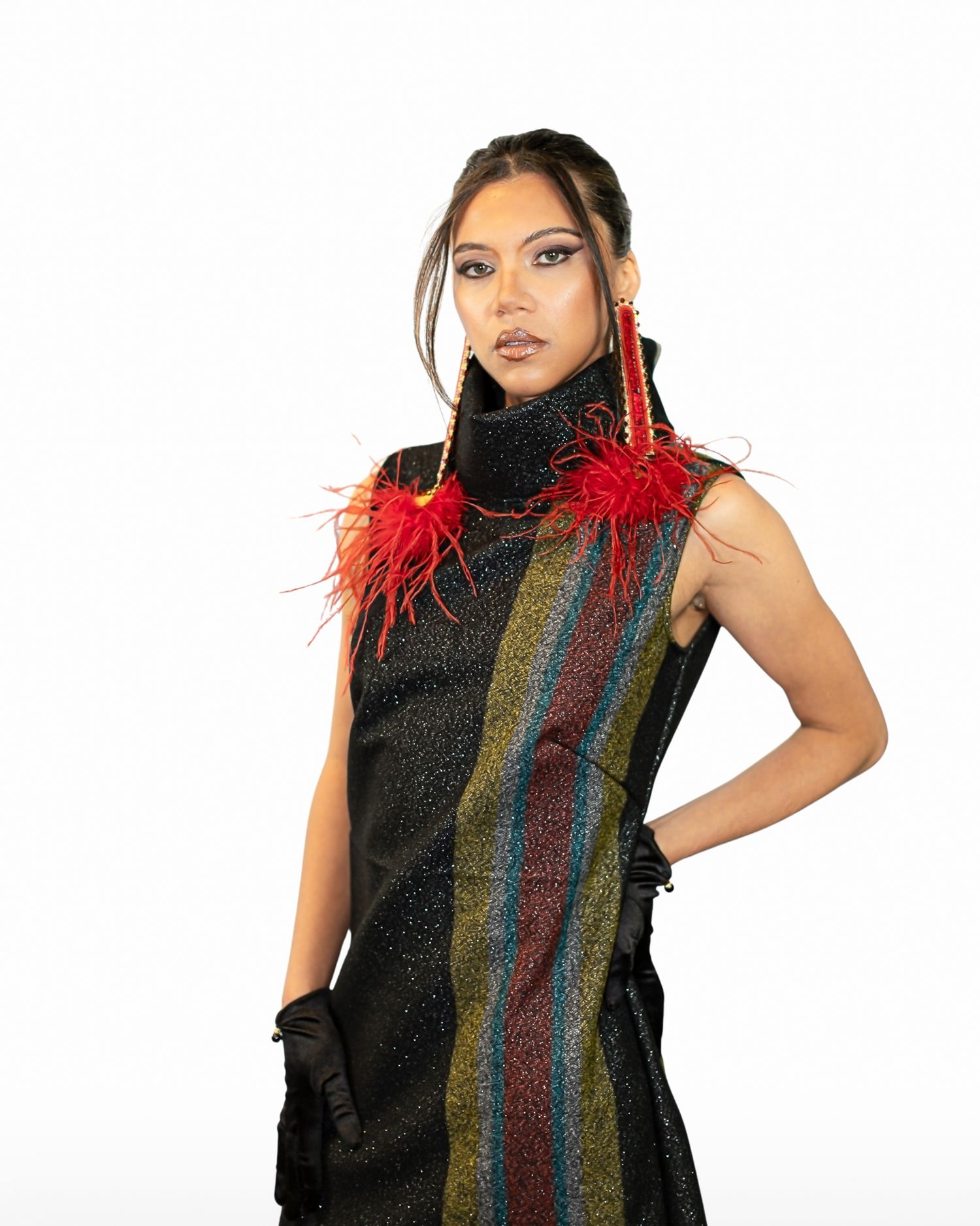 Model wearing black multicolor striped sleeveless turtleneck dress with dramatic red feather earrings and black gloves.