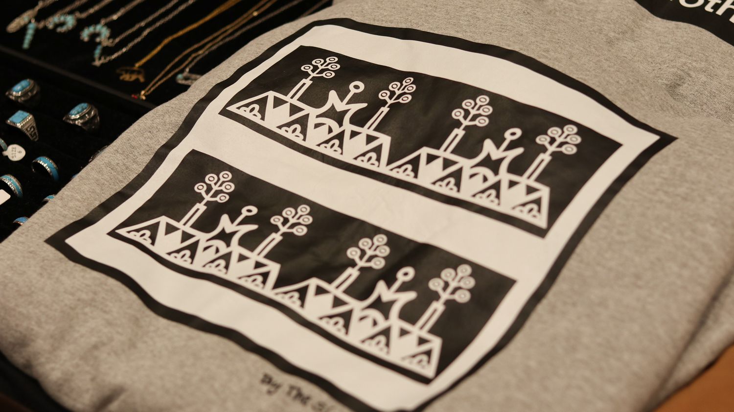 Gray t-shirt featuring a bold black and white geometric tribal pattern print with symmetrical designs.