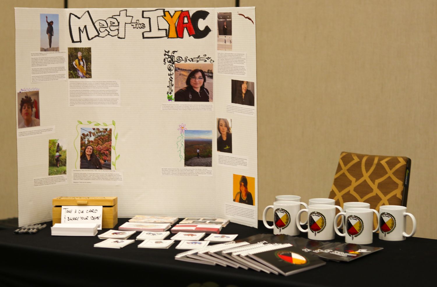 IYAC meet the team display board with photos, mugs, and promotional materials on a black table.