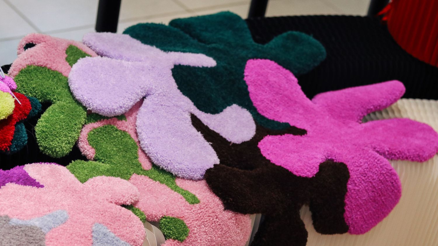Colorful tufted floral shaped rugs in pink, purple, green, and dark red displayed on a floor.