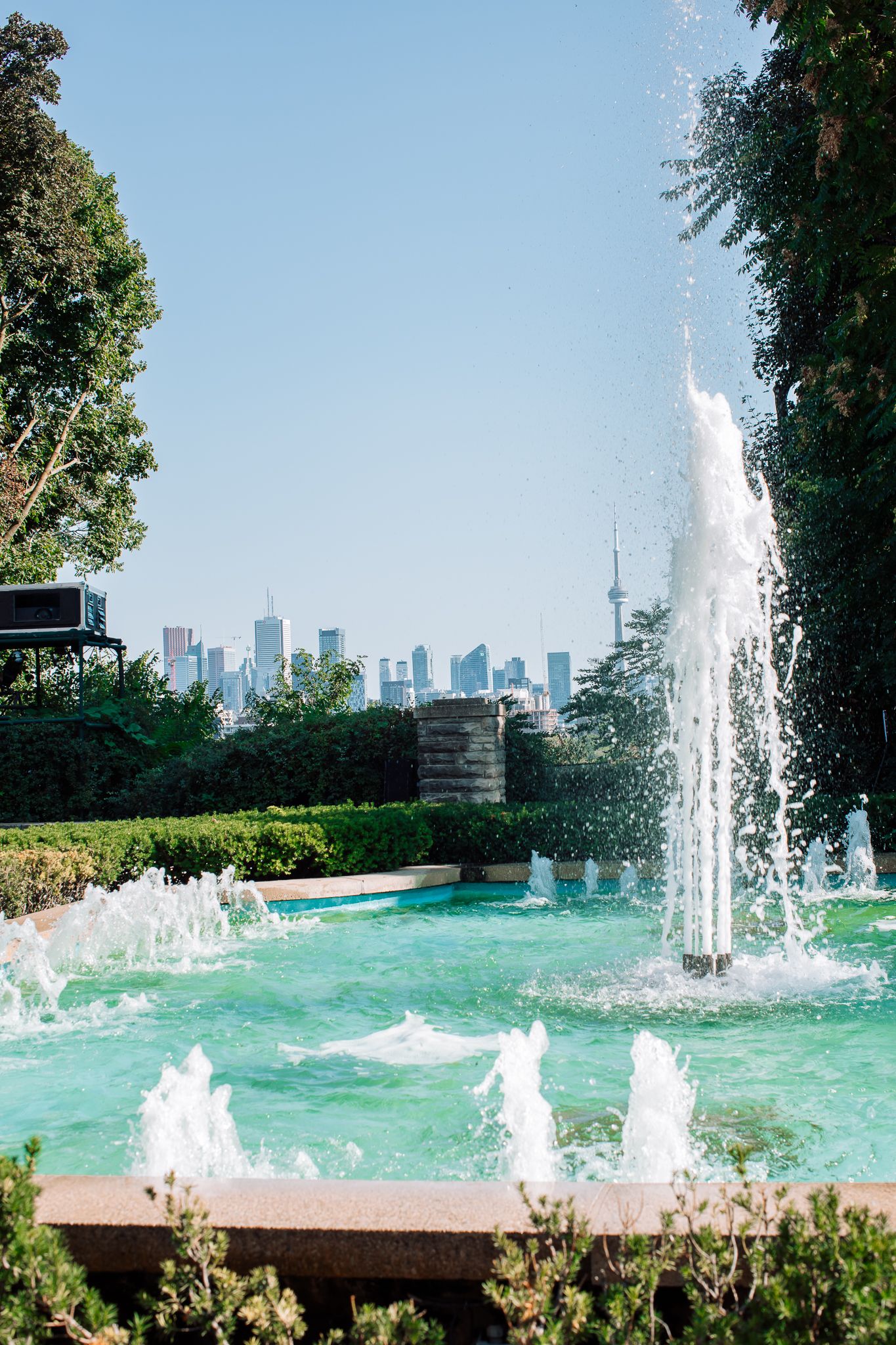 Fountain with turquoise water in Toronto park with CN Tower city skyline visible in background.