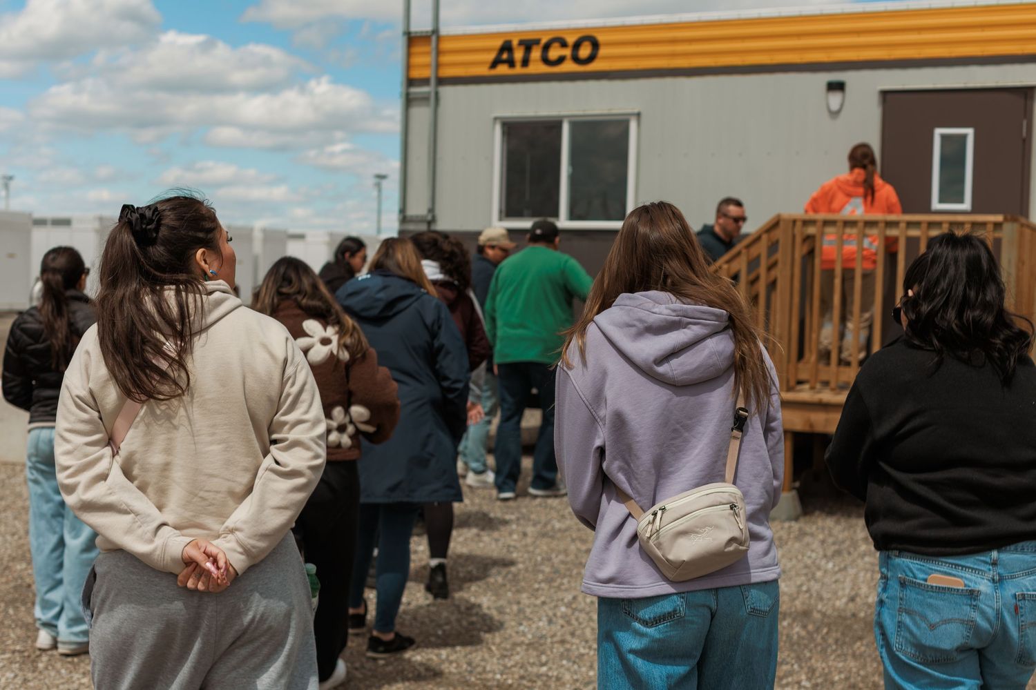 Group of students visiting an ATCO facility, listening to a presenter on outdoor steps during a site tour.