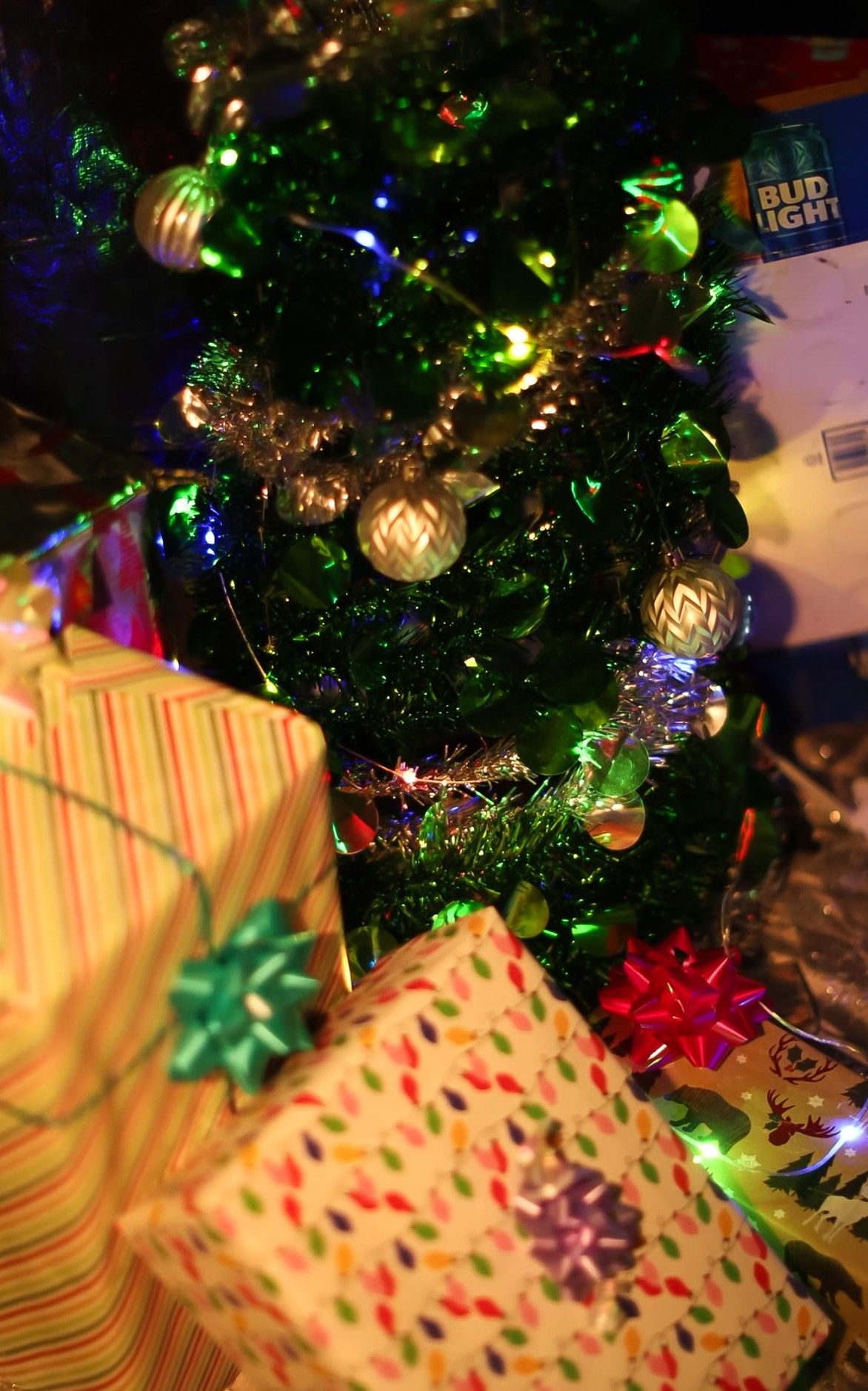 Christmas tree with colorful lights and wrapped presents underneath against dark background.