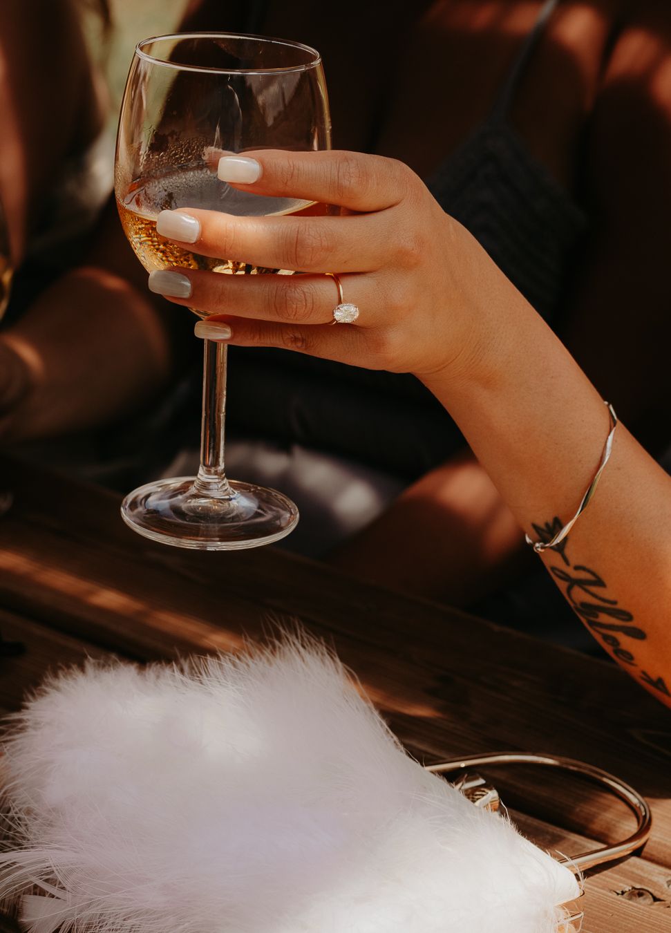 Close-up of hands holding wine glasses with white feather decor on wooden surface.