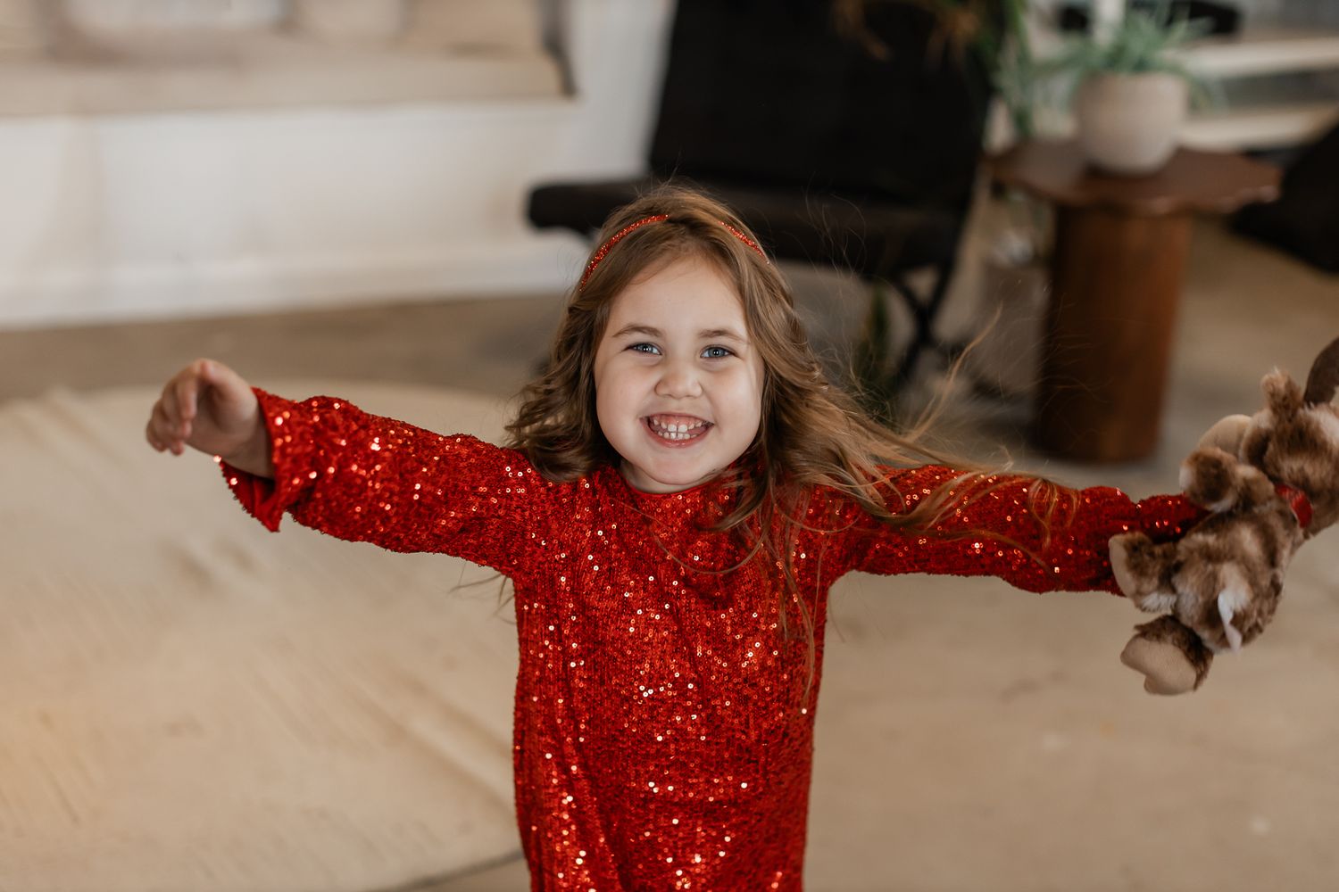 Child in sparkly red dress twirling and dancing during holiday photoshoot.